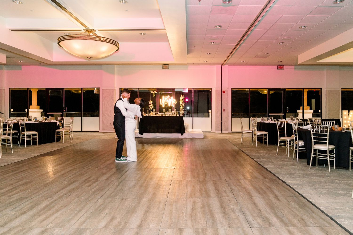 A couple shares a romantic slow dance in an elegant ballroom with pink ambient lighting.