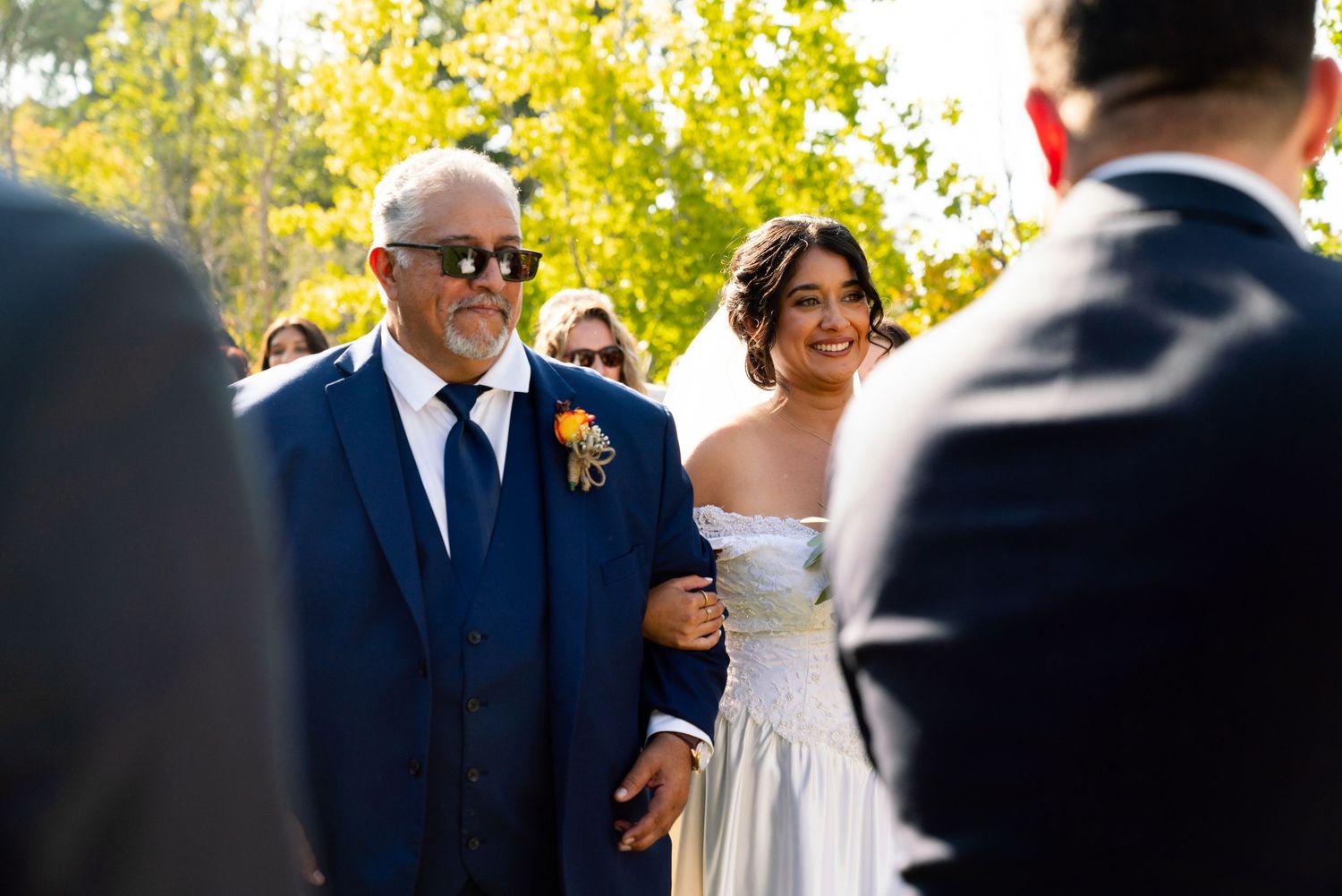 A joyful wedding processional moment outdoors on a sunny autumn day with trees in the background.
