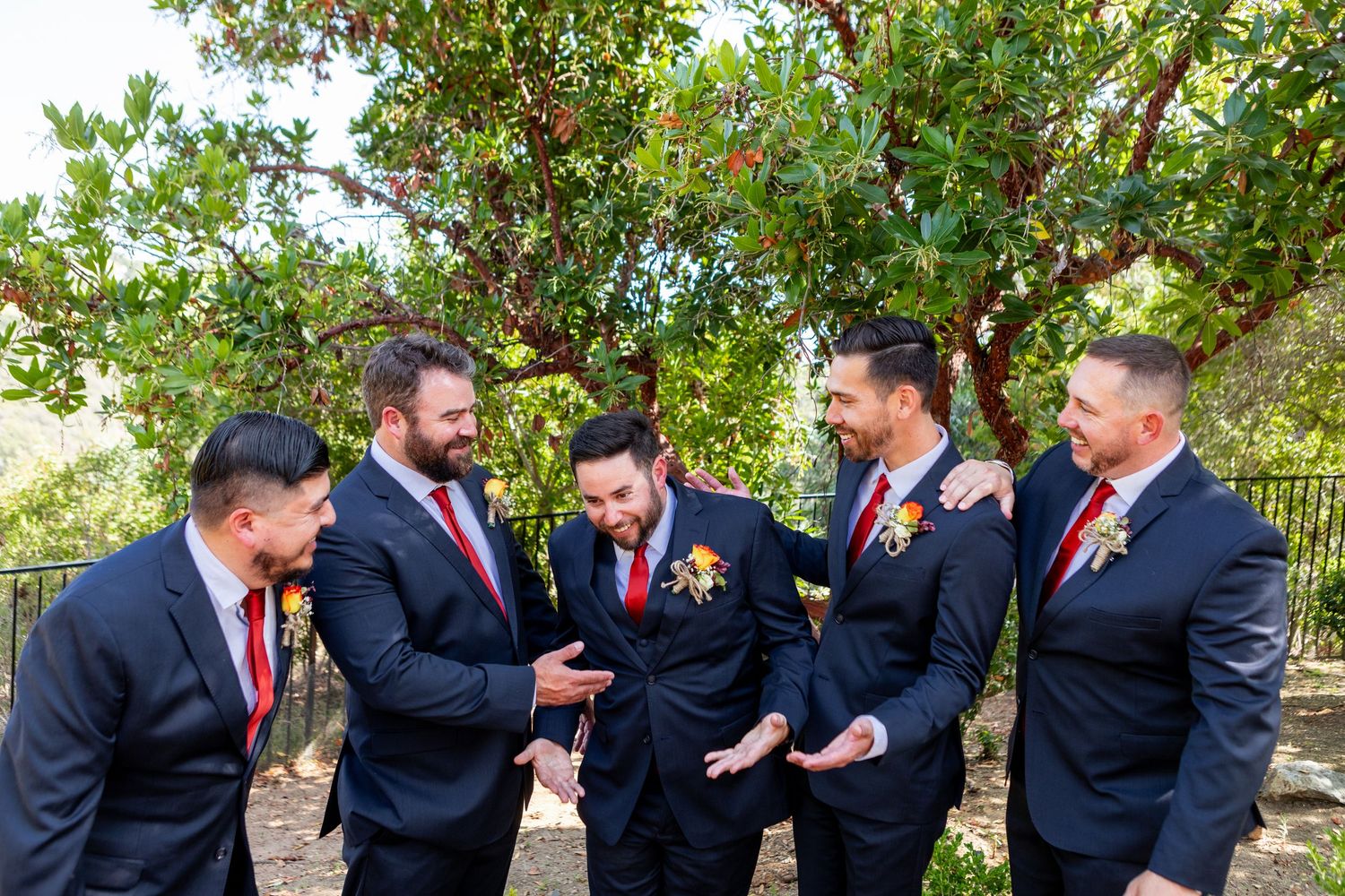 Groomsmen in navy suits with red ties sharing a laugh together outdoors.