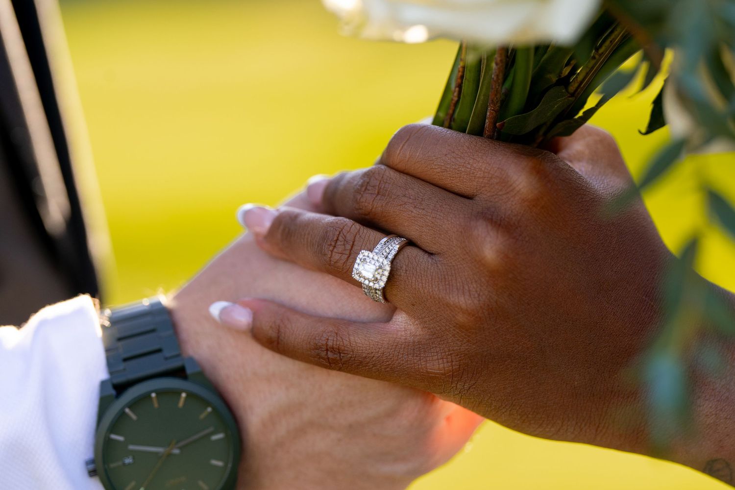 Close-up of engagement ring and watch hands holding wedding bouquet.