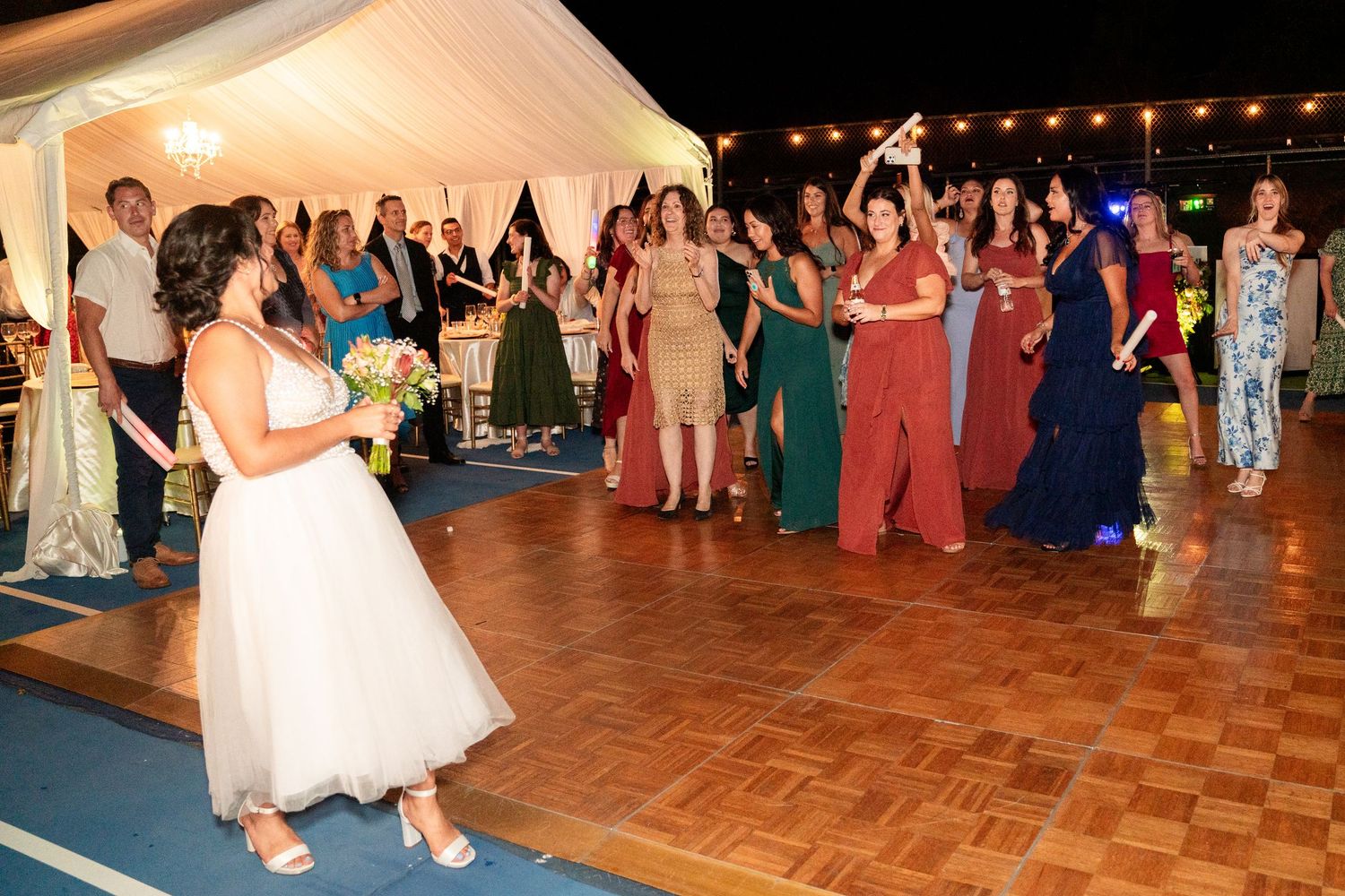 Bride tossing bouquet to waiting crowd of guests on dance floor at wedding reception.