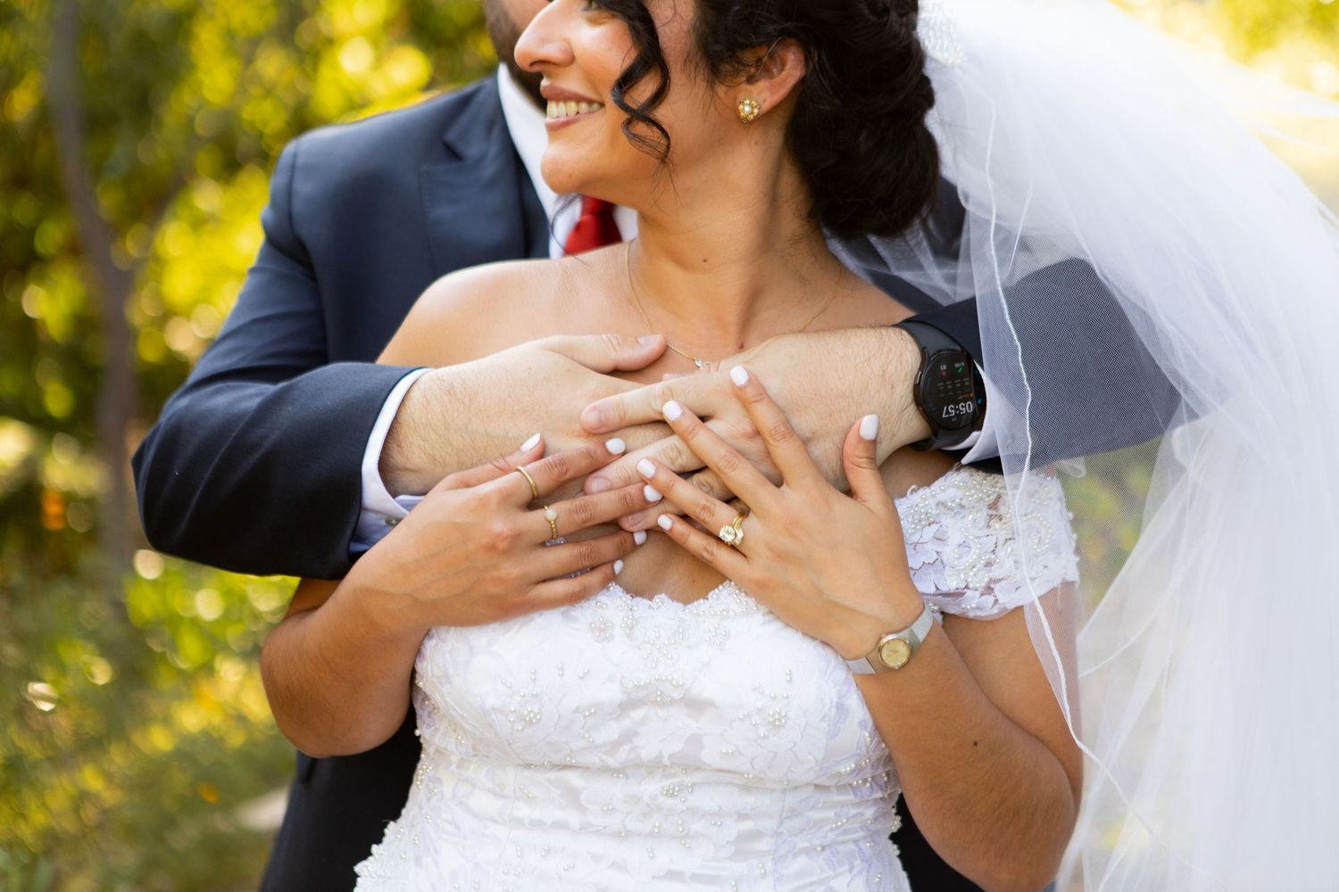 Close-up of hands showing wedding rings against white lace dress.