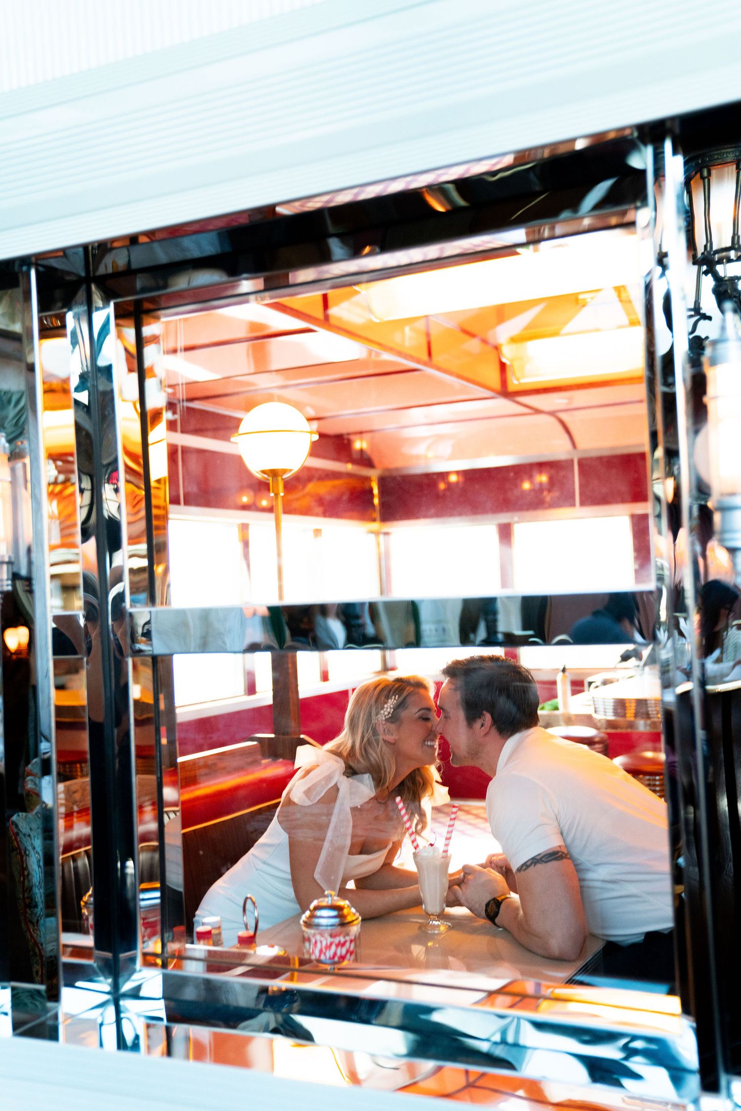 Two people sharing an intimate moment at a retro diner booth illuminated by warm lighting through window reflections.