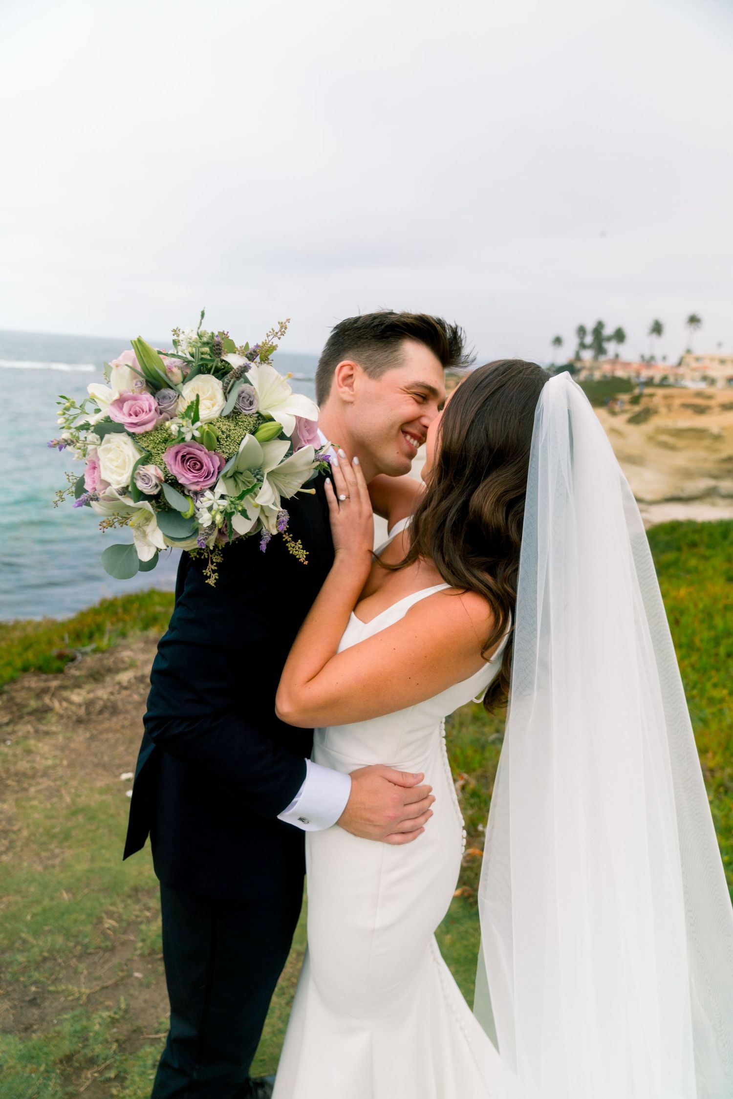 A romantic wedding moment on a cliff overlooking the ocean with a beautiful floral bouquet in hand.