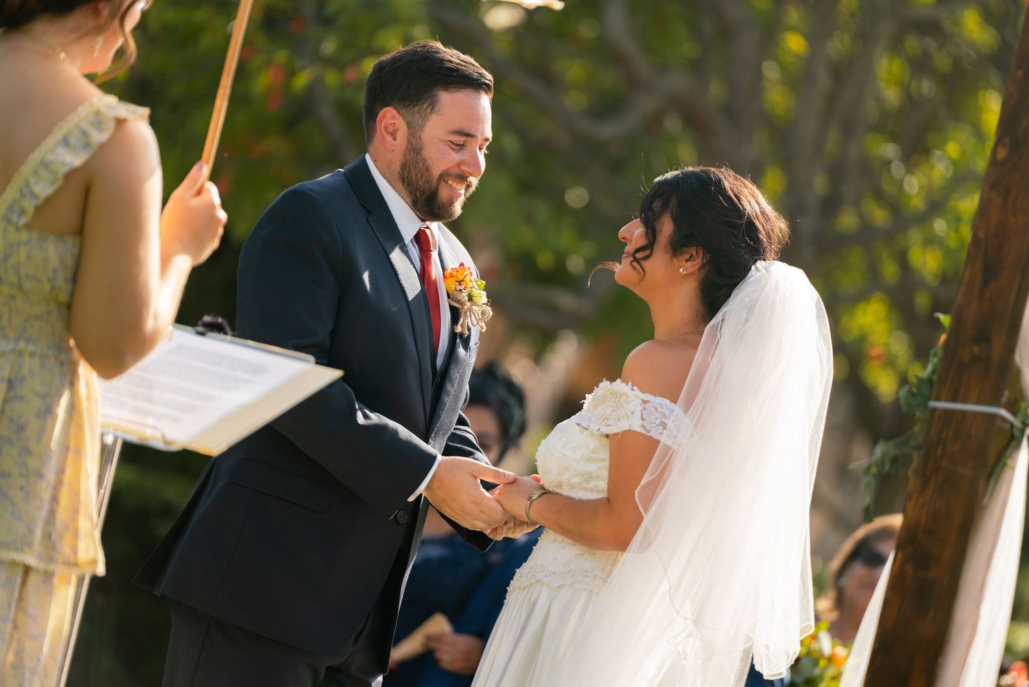 A wedding ceremony taking place outdoors with attendees gathered under natural lighting.