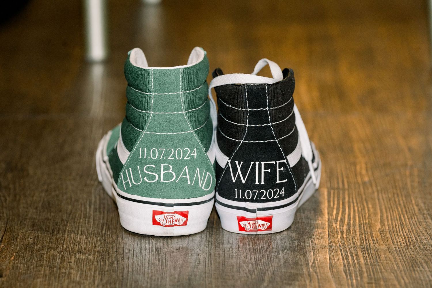 Custom Vans sneakers decorated with 'Husband' and 'Wife' text and wedding date showing back view on wooden floor.