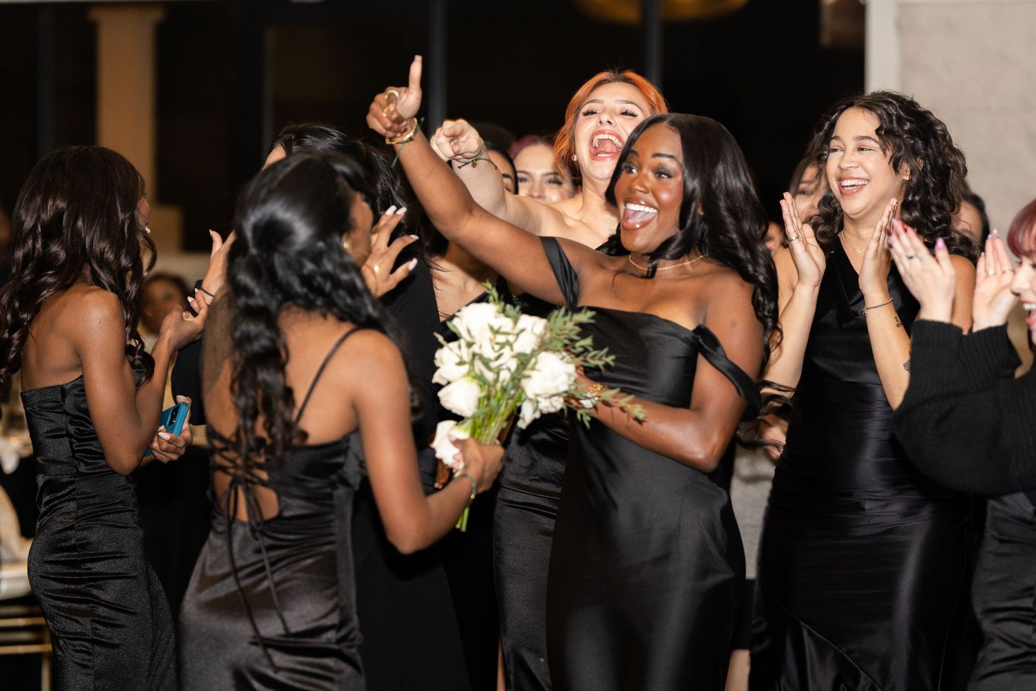 Bridesmaids in black dresses celebrating joyfully with the bouquet.