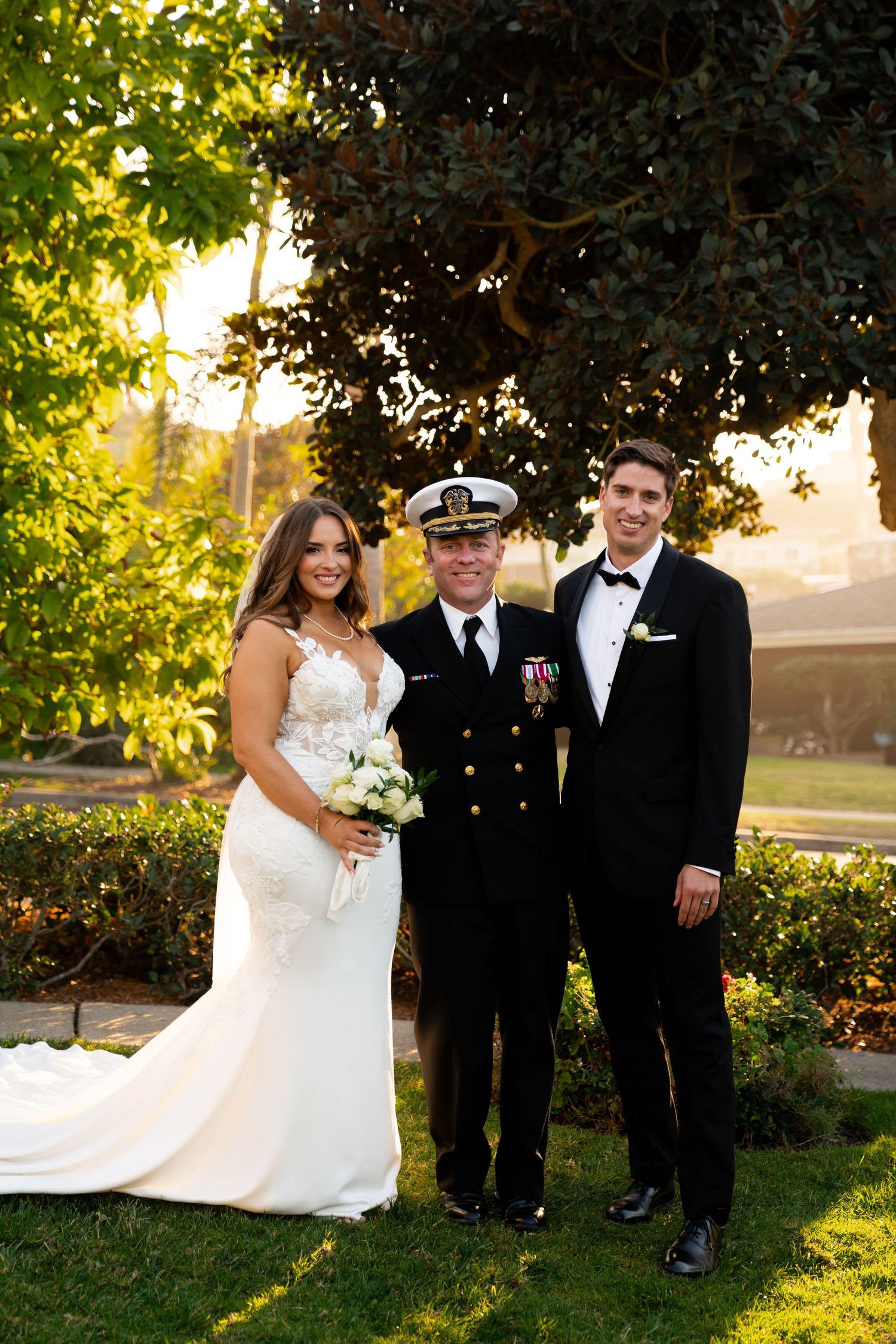 Wedding party posing under trees at sunset with military officer officiating.