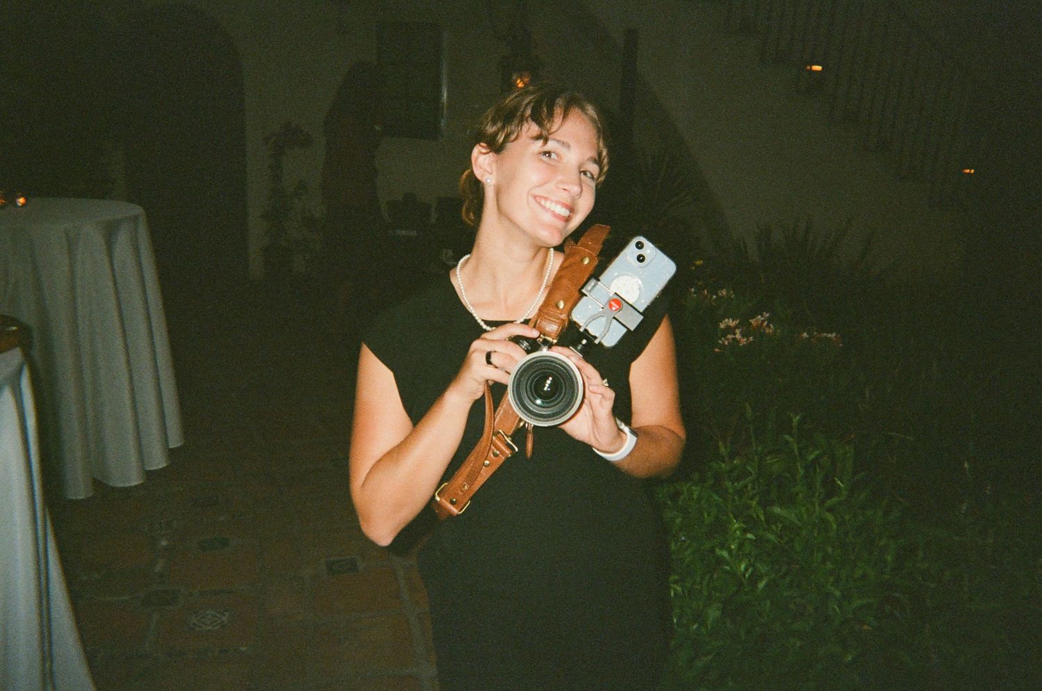 A person holding a vintage camera at night in a casual outdoor setting.