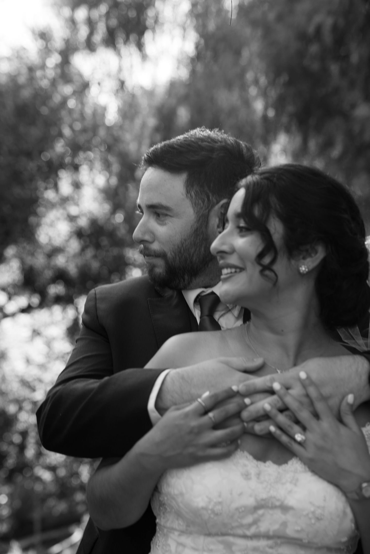 Black and white portrait captures tender embrace between newlyweds in outdoor setting.