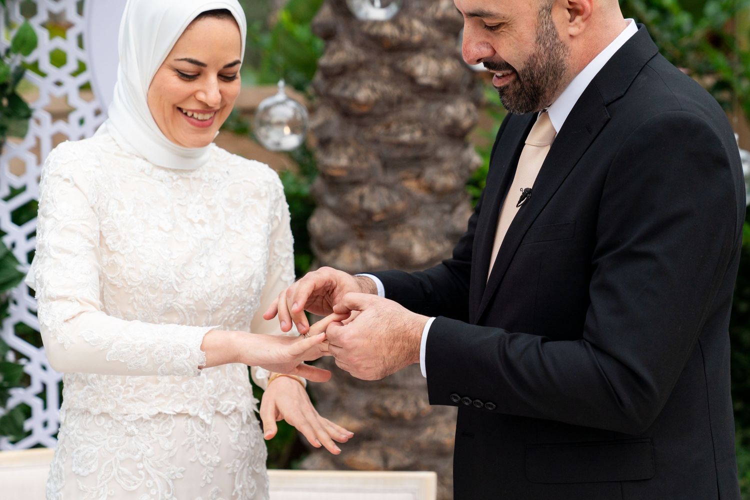 A couple shares an intimate wedding ceremony moment exchanging rings against a stone wall backdrop.