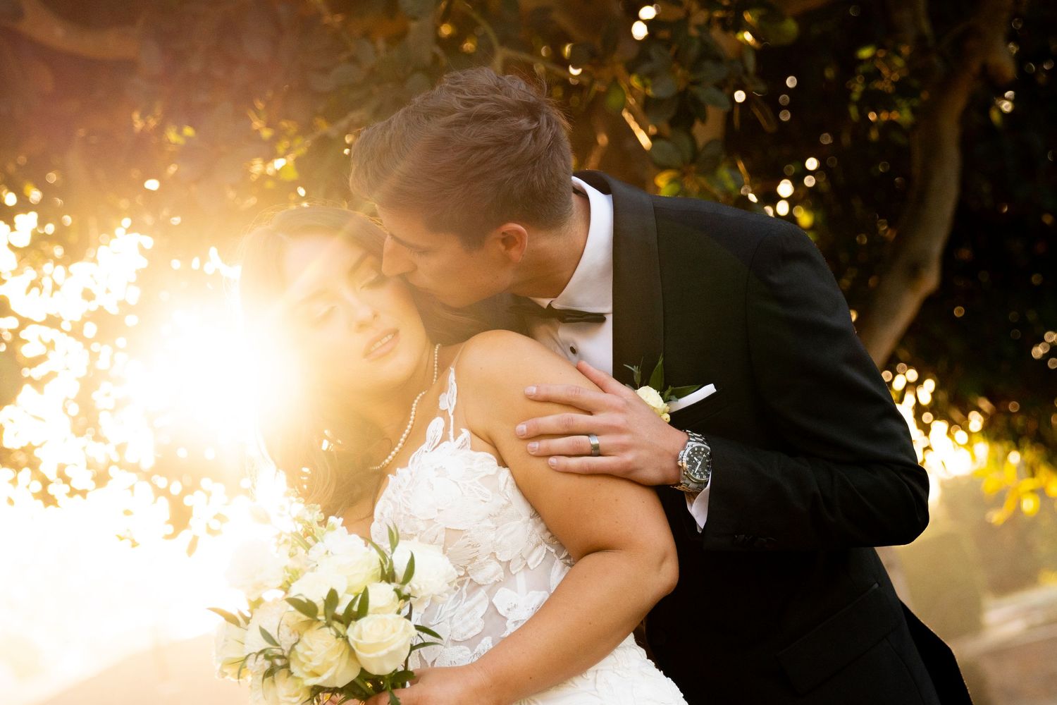 Newlyweds share an intimate moment during golden hour with white bouquet.
