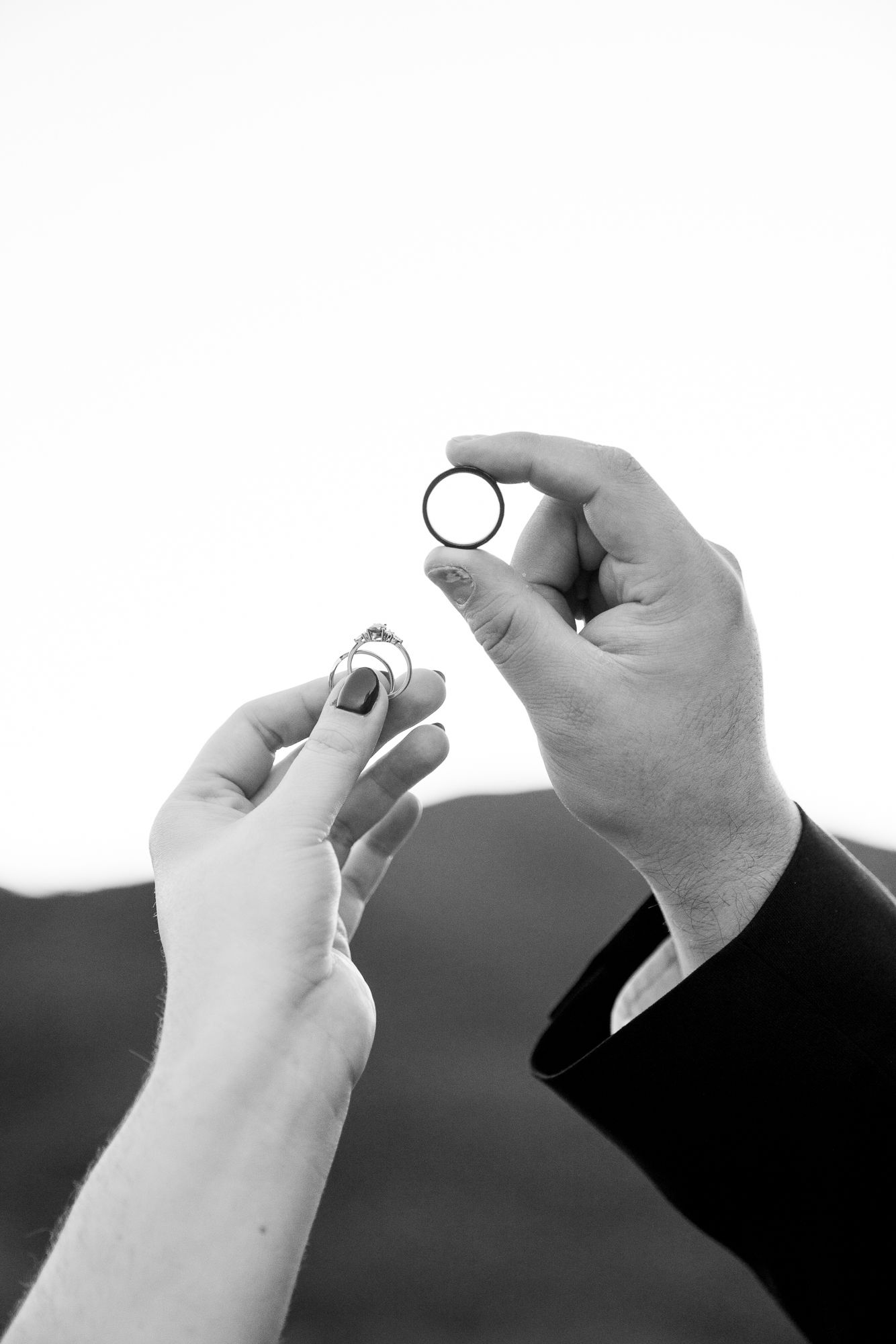 Two hands in black and white photograph holding wedding rings against a blurred background.