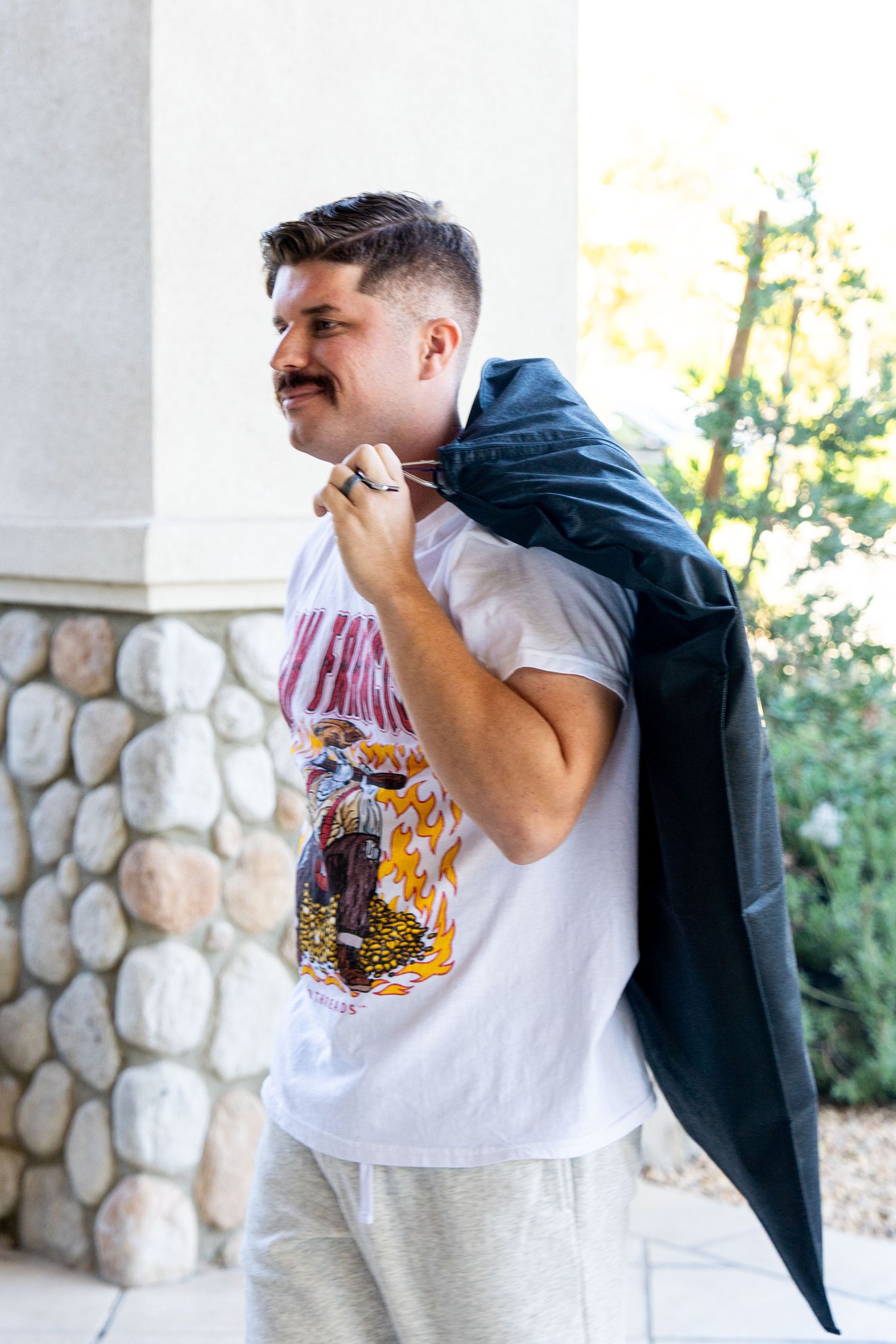 A person wearing a graphic t-shirt and hoodie poses against a stone wall outdoors.
