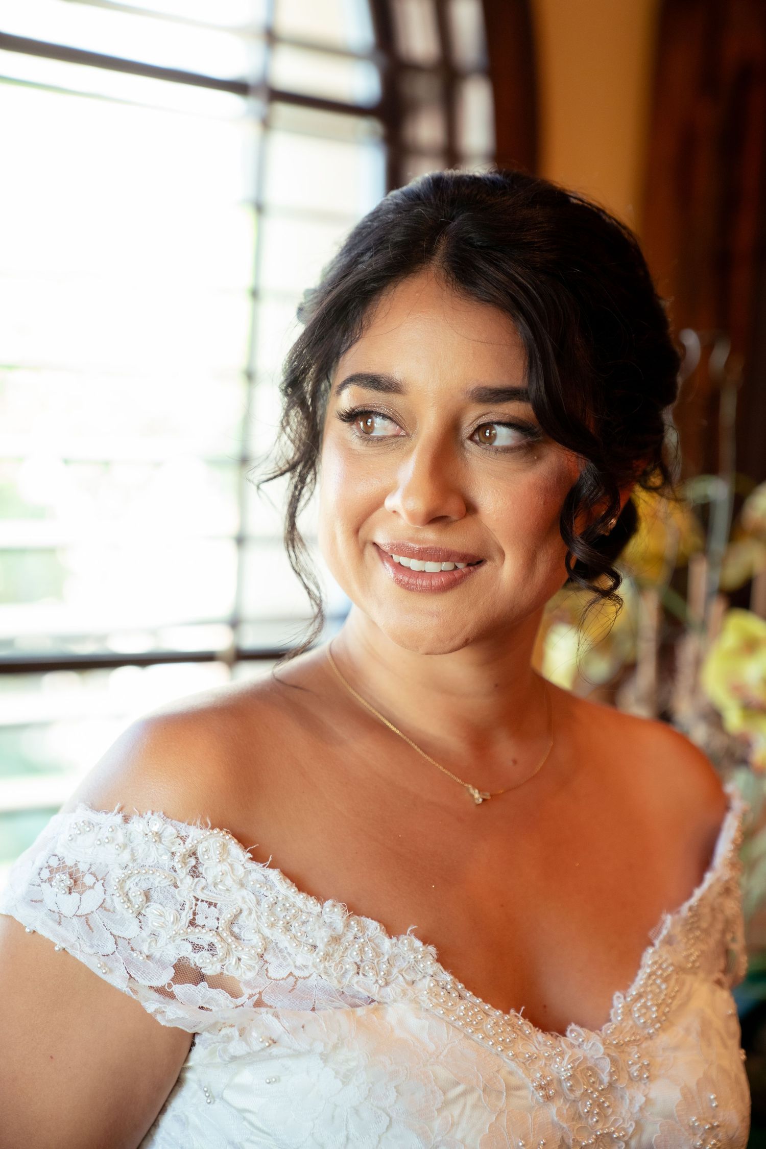 Close up portrait of a bride in lace off-shoulder wedding dress with natural makeup and dark updo hairstyle.