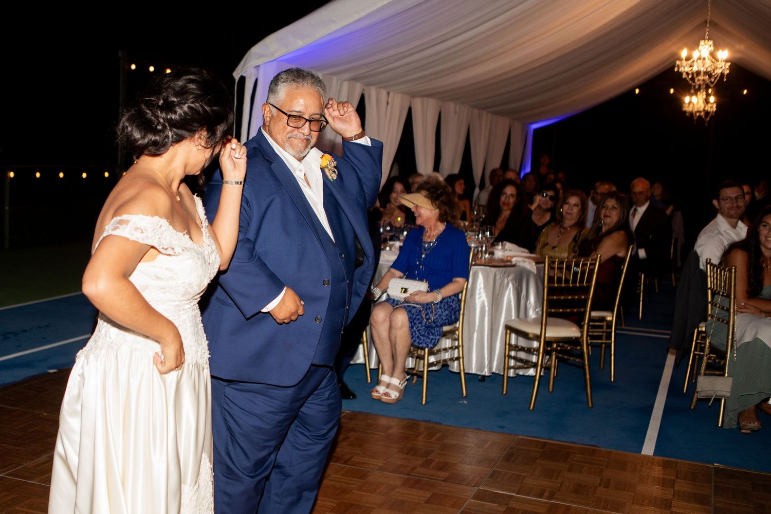 A celebratory dance moment on a blue-floored reception area under an elegant white tent.