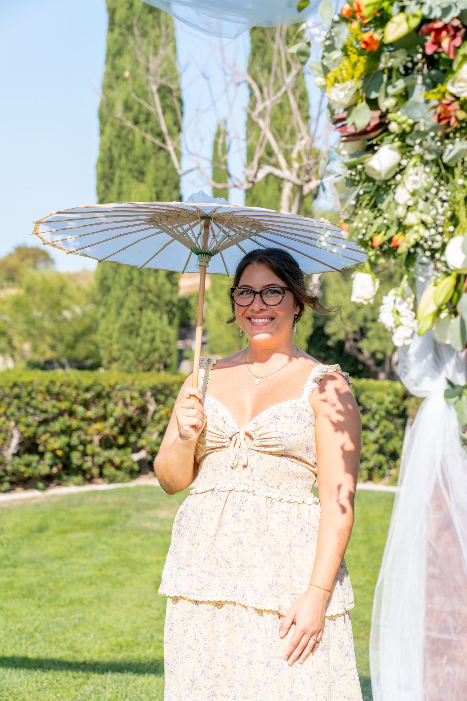 A person holds a decorative white parasol at an outdoor garden wedding with floral decorations.