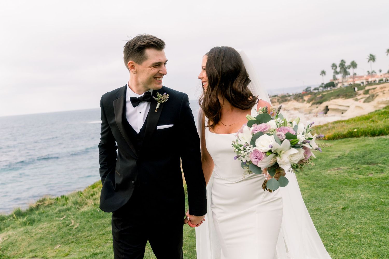 A bride and groom share a loving moment on a coastal cliff overlooking the ocean on their wedding day.