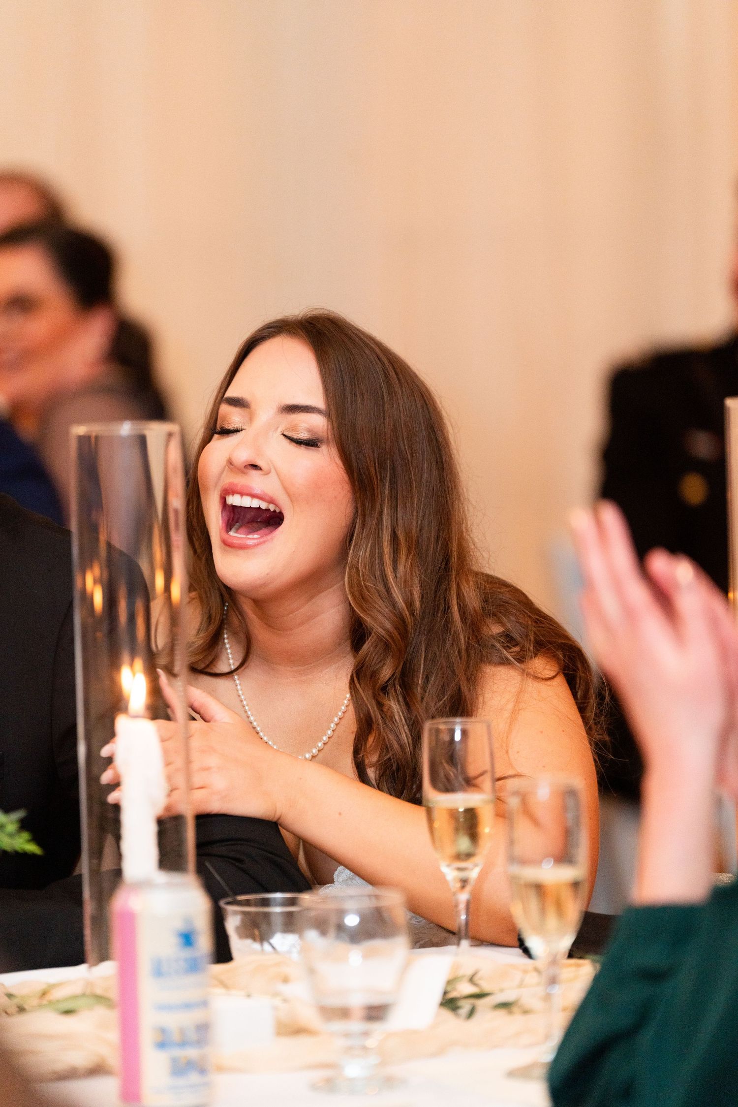 A wedding guest laughs joyfully during the reception dinner with champagne glasses on the table.