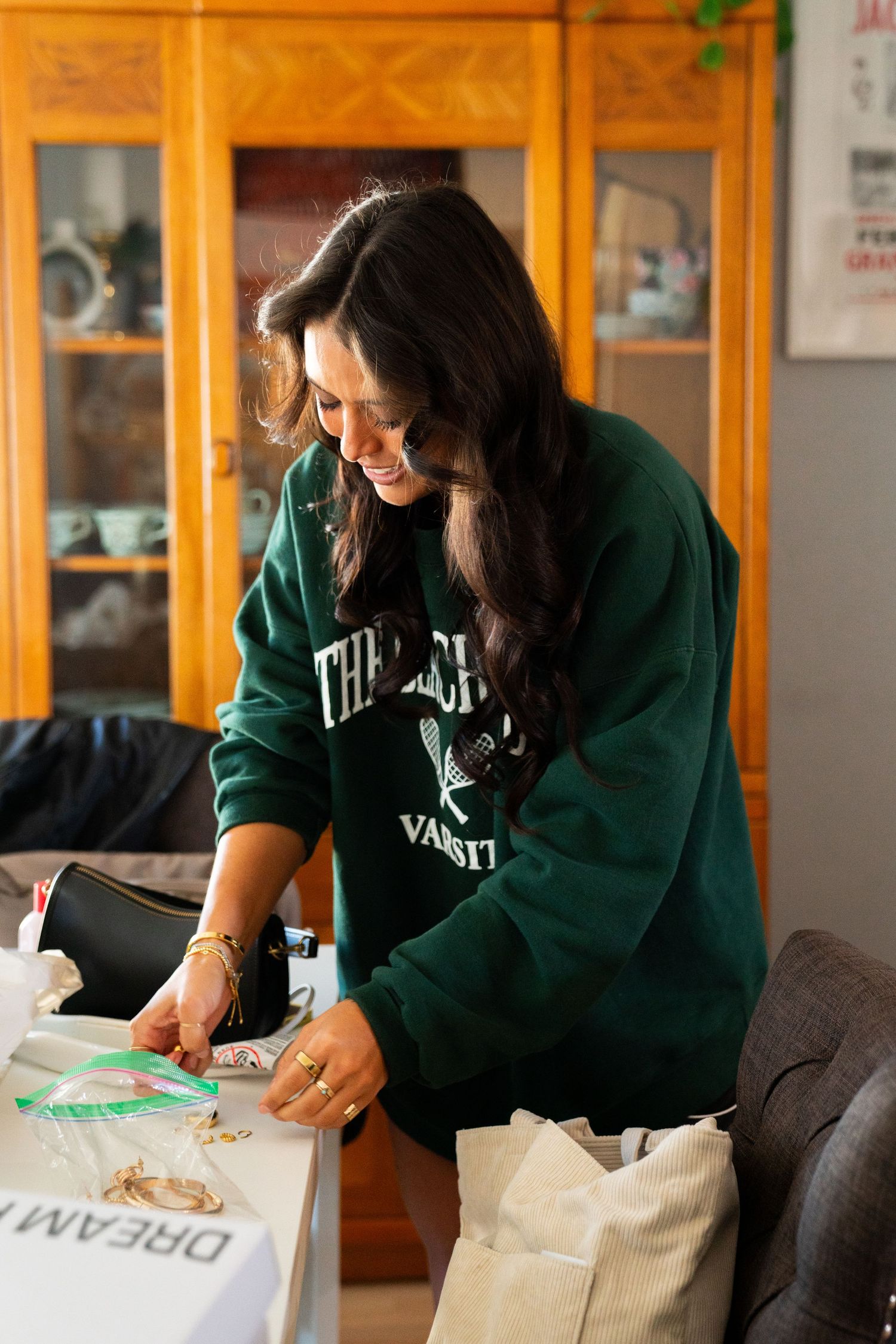 A figure in a green university sweatshirt works on craft materials at a wooden table.