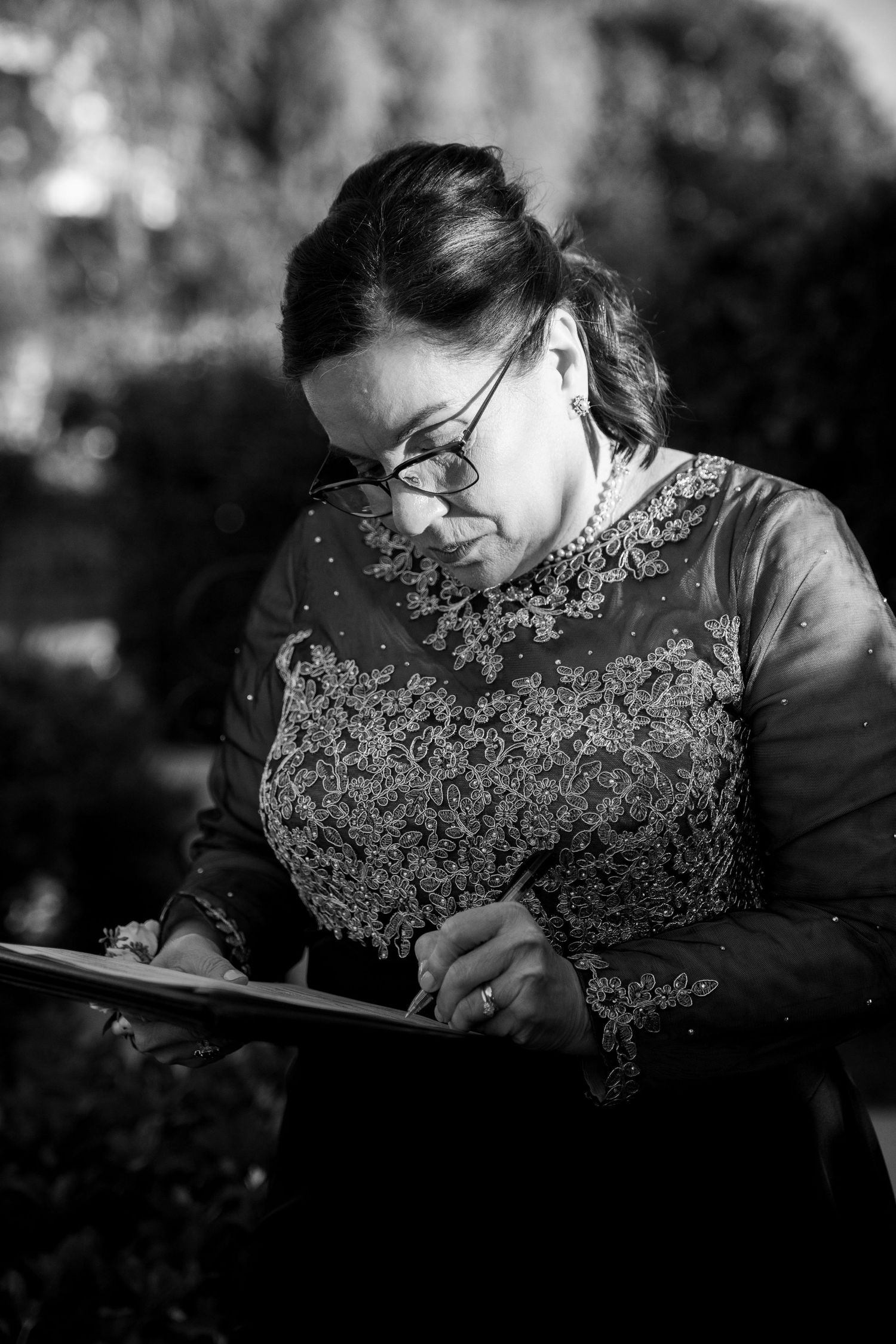 Black and white portrait of someone writing on clipboard while wearing an elegant lace dress.