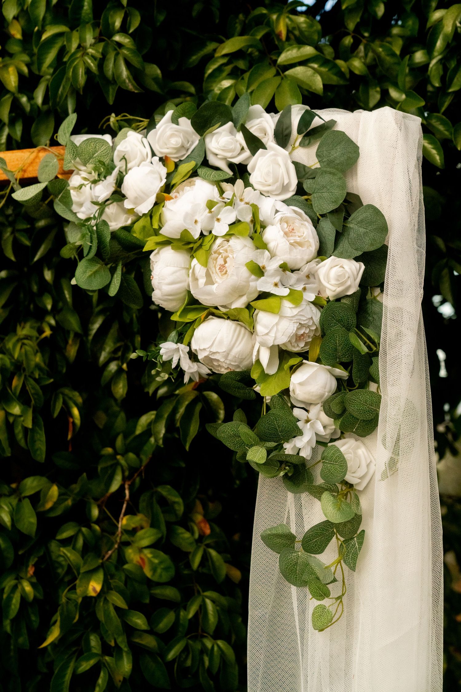 White roses and eucalyptus leaves arranged on white tulle fabric against a green foliage background.