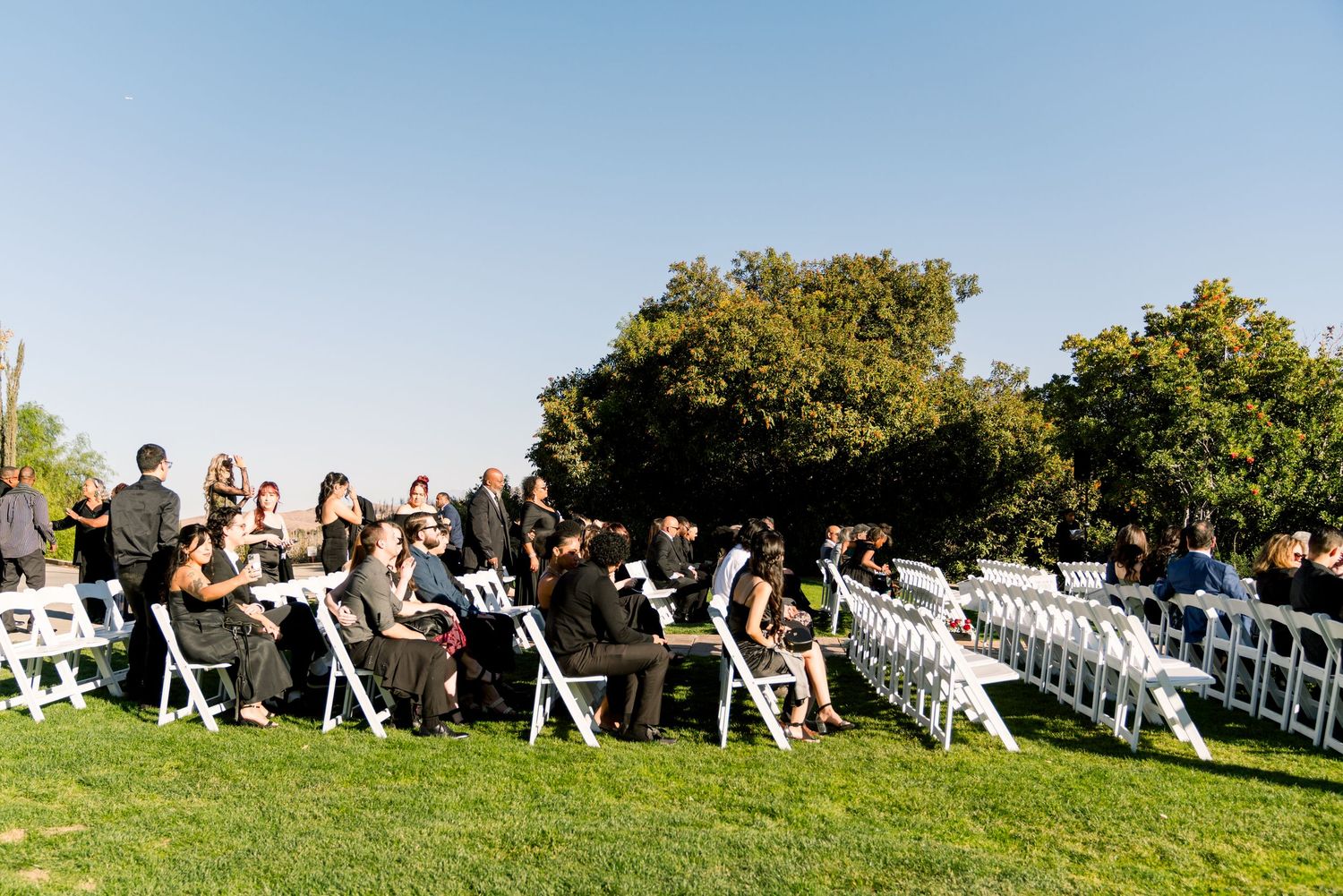 Outdoor wedding ceremony setup with guests seated in white chairs on a lush green lawn.
