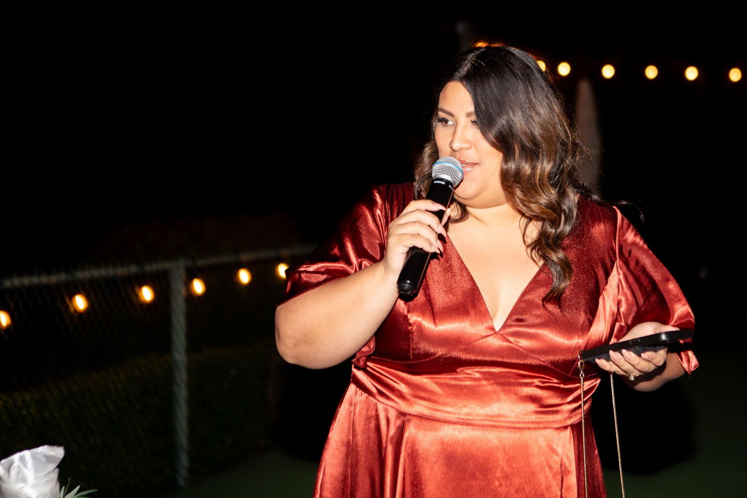 Evening wedding reception speech being given outdoors under string lights.