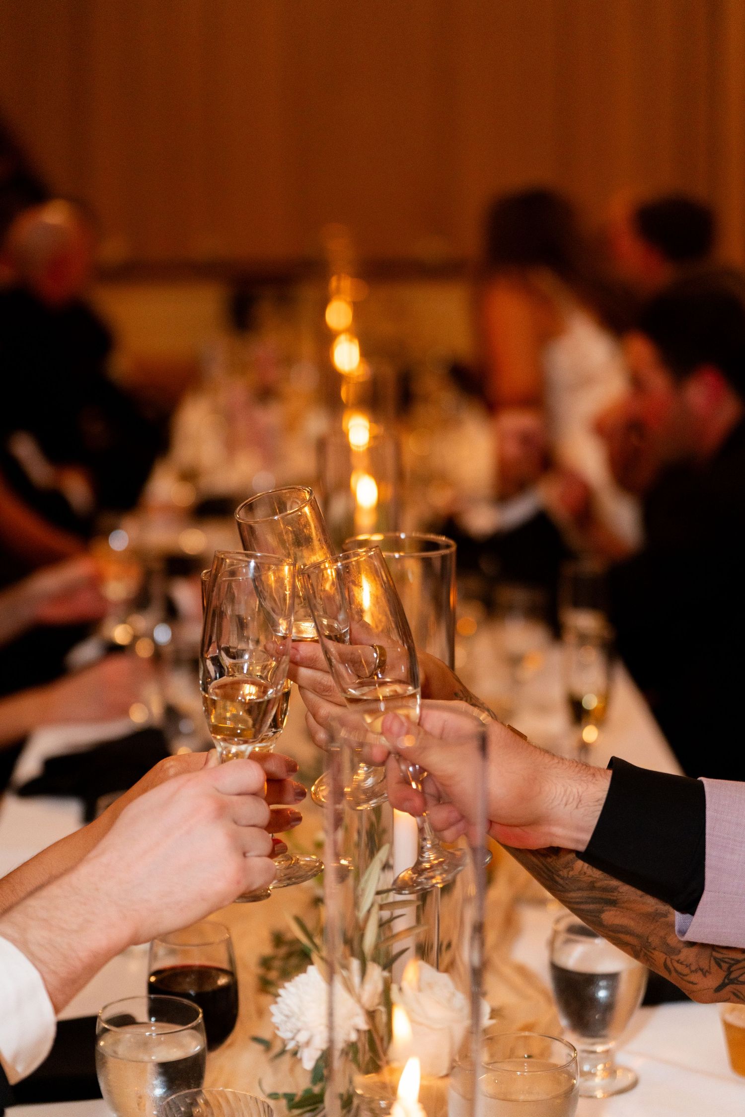 Wedding guests raising champagne glasses for a toast at an elegant candlelit reception dinner.