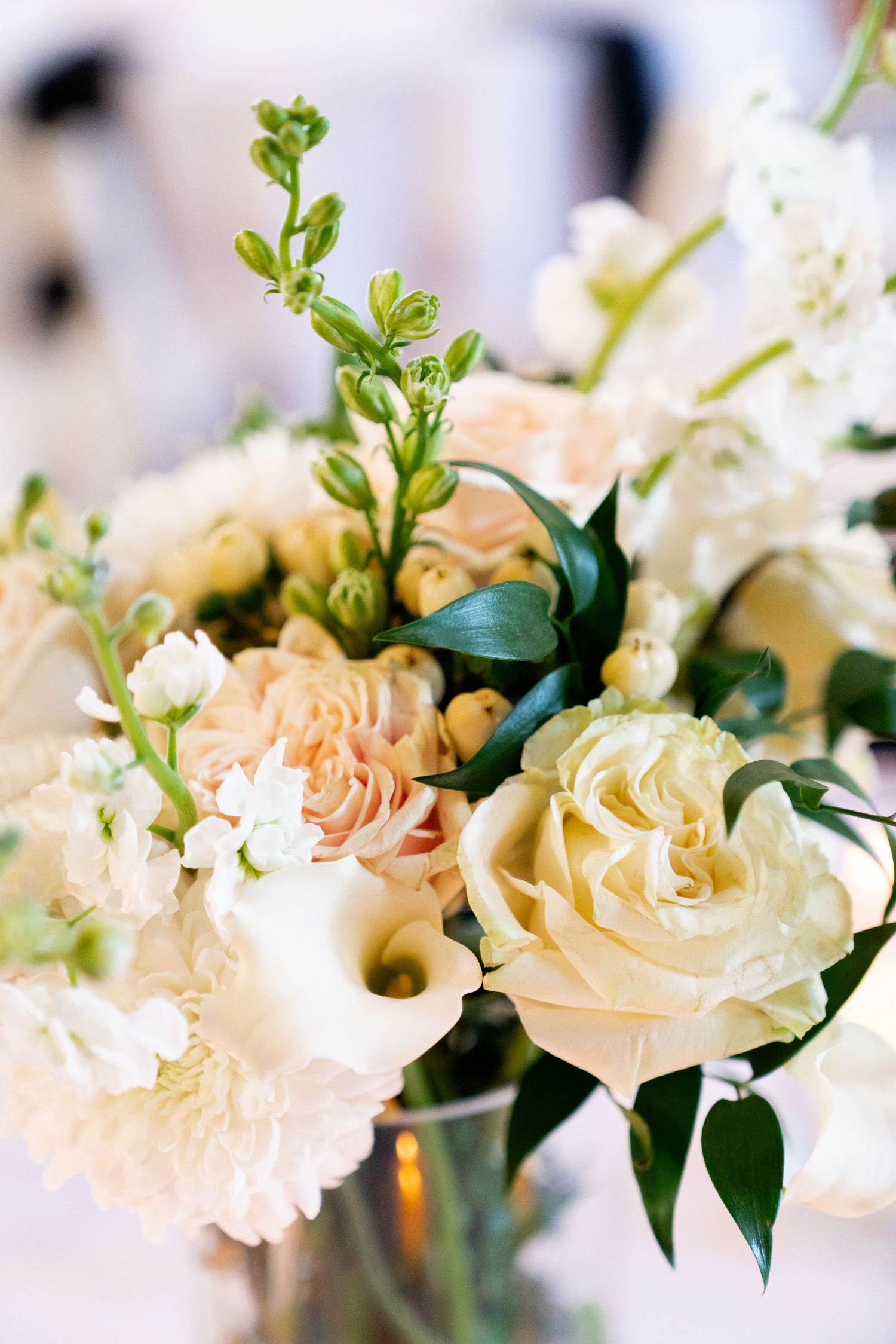 A delicate floral arrangement featuring peach and cream roses with greenery in a vase against a soft blurred background.