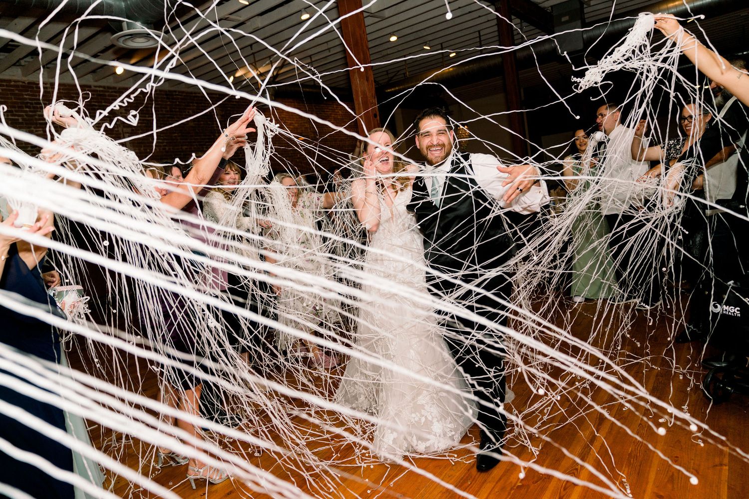 People celebrate at a nighttime wedding event with streamer decorations creating dramatic white lines across the dark space.