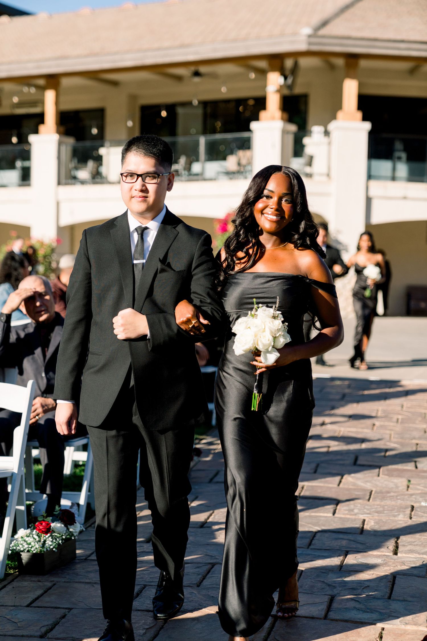 Wedding party members walking down a paved path at an outdoor venue.