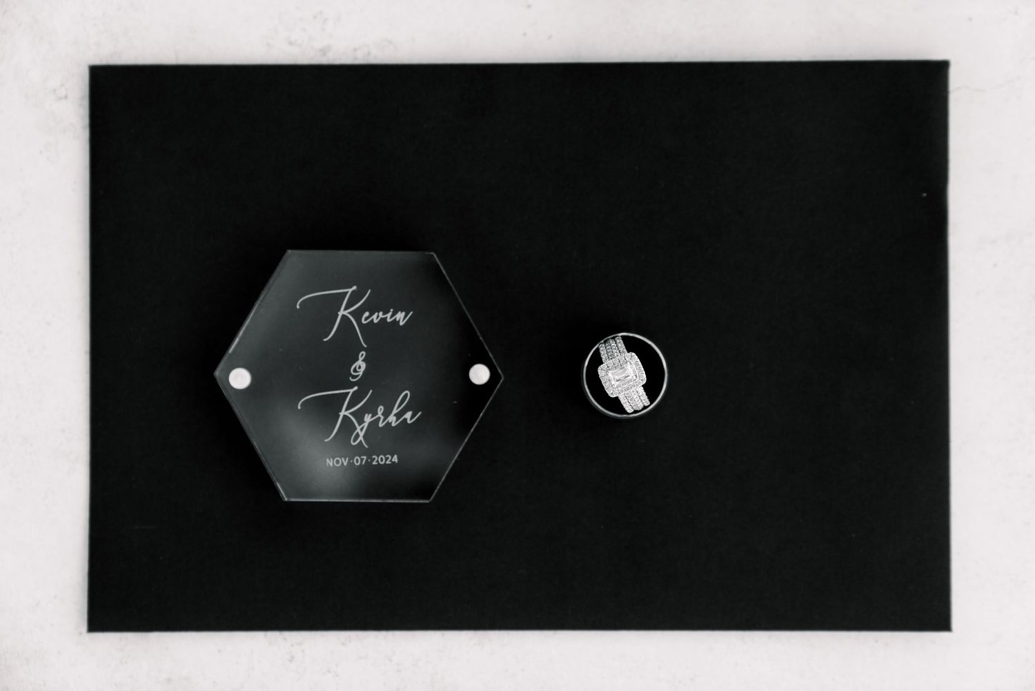 Black and white photo of hexagonal wedding details and ring on dark background.