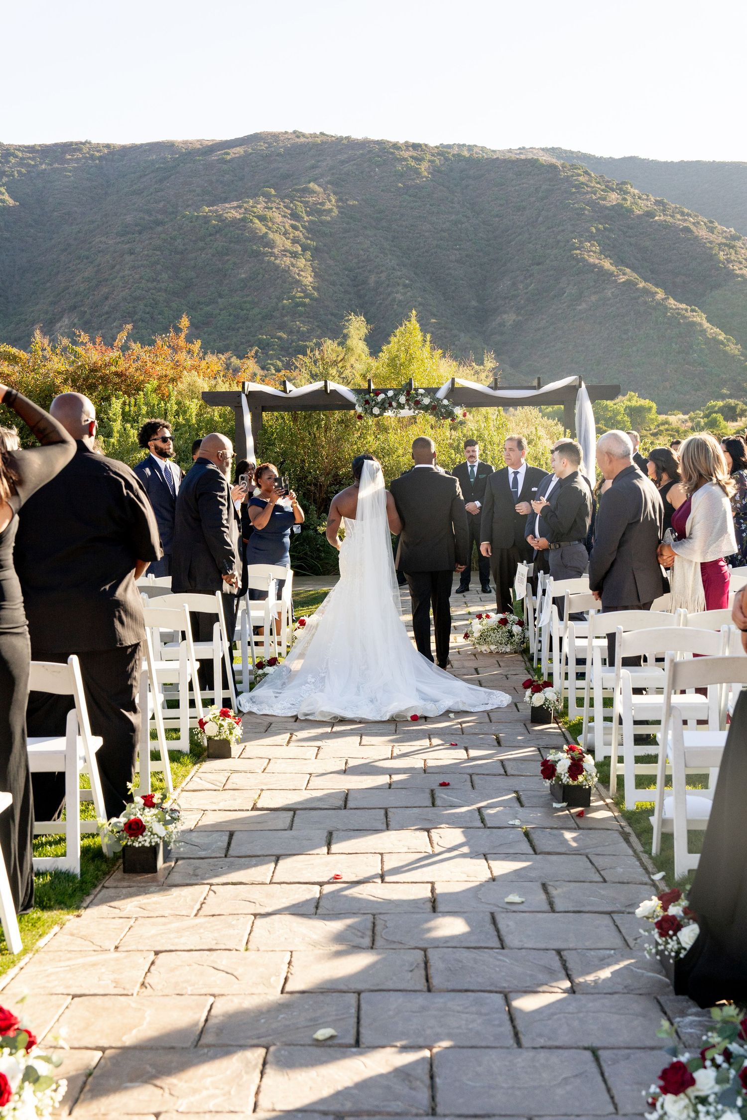 Wedding ceremony setup with white chairs and stone pathway leading to mountain backdrop in outdoor venue.