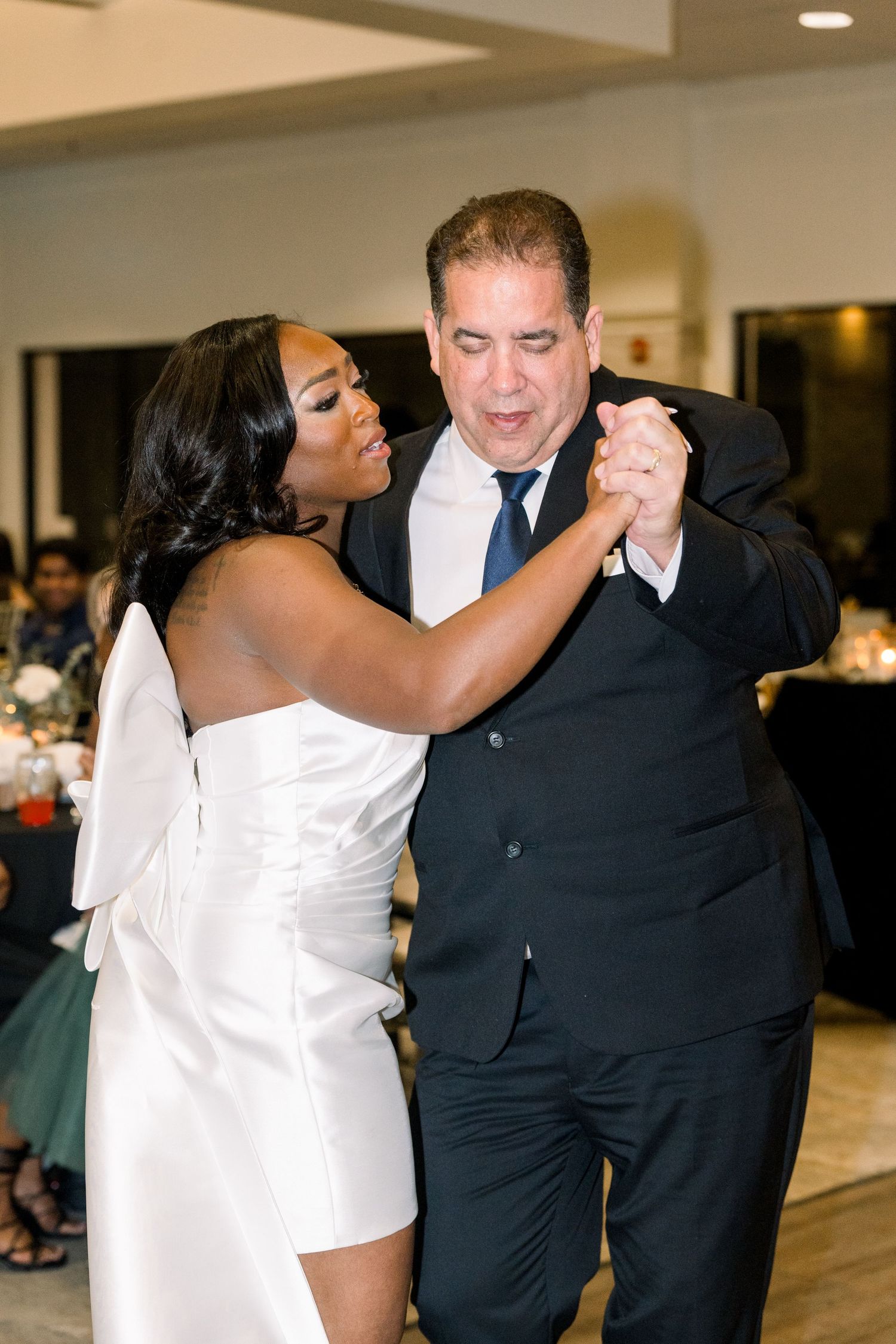 A couple dances together at a wedding reception in formal attire.