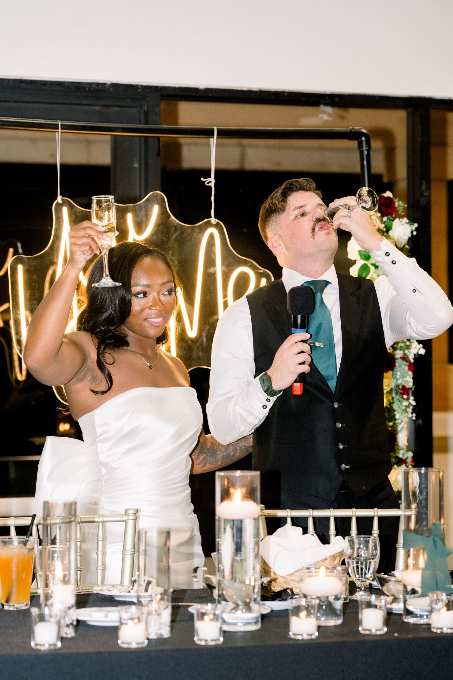 Wedding couple toasts and celebrates at their reception under neon lighting.