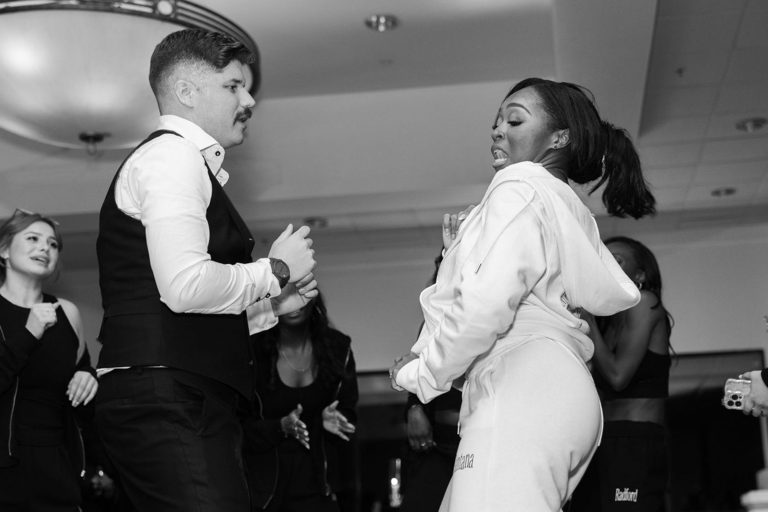 Wedding guests dance together in formal attire during a black and white reception moment.