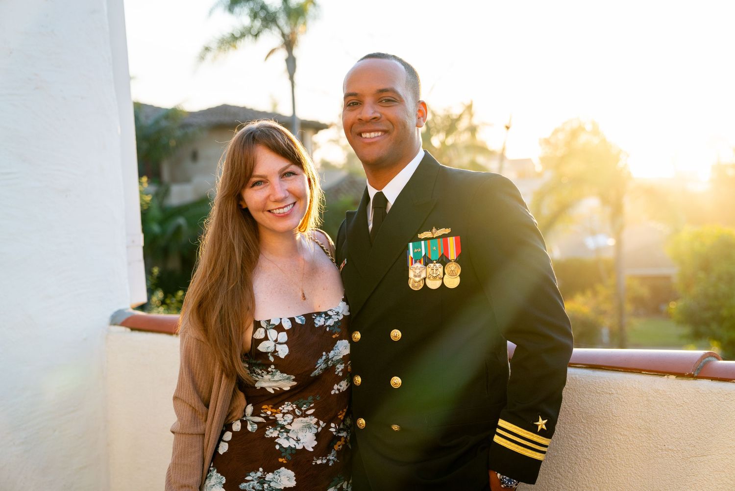 Happy military couple pose together at sunset, officer in dress uniform with medals.