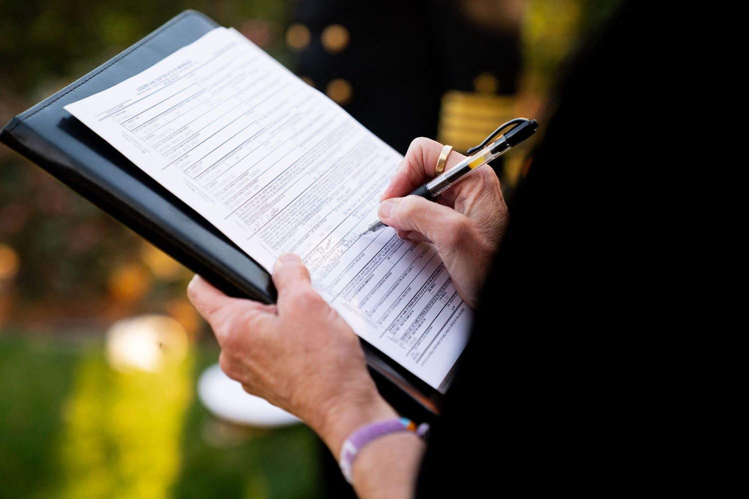 Close-up of hands holding a pen and clipboard with wedding ceremony documents.