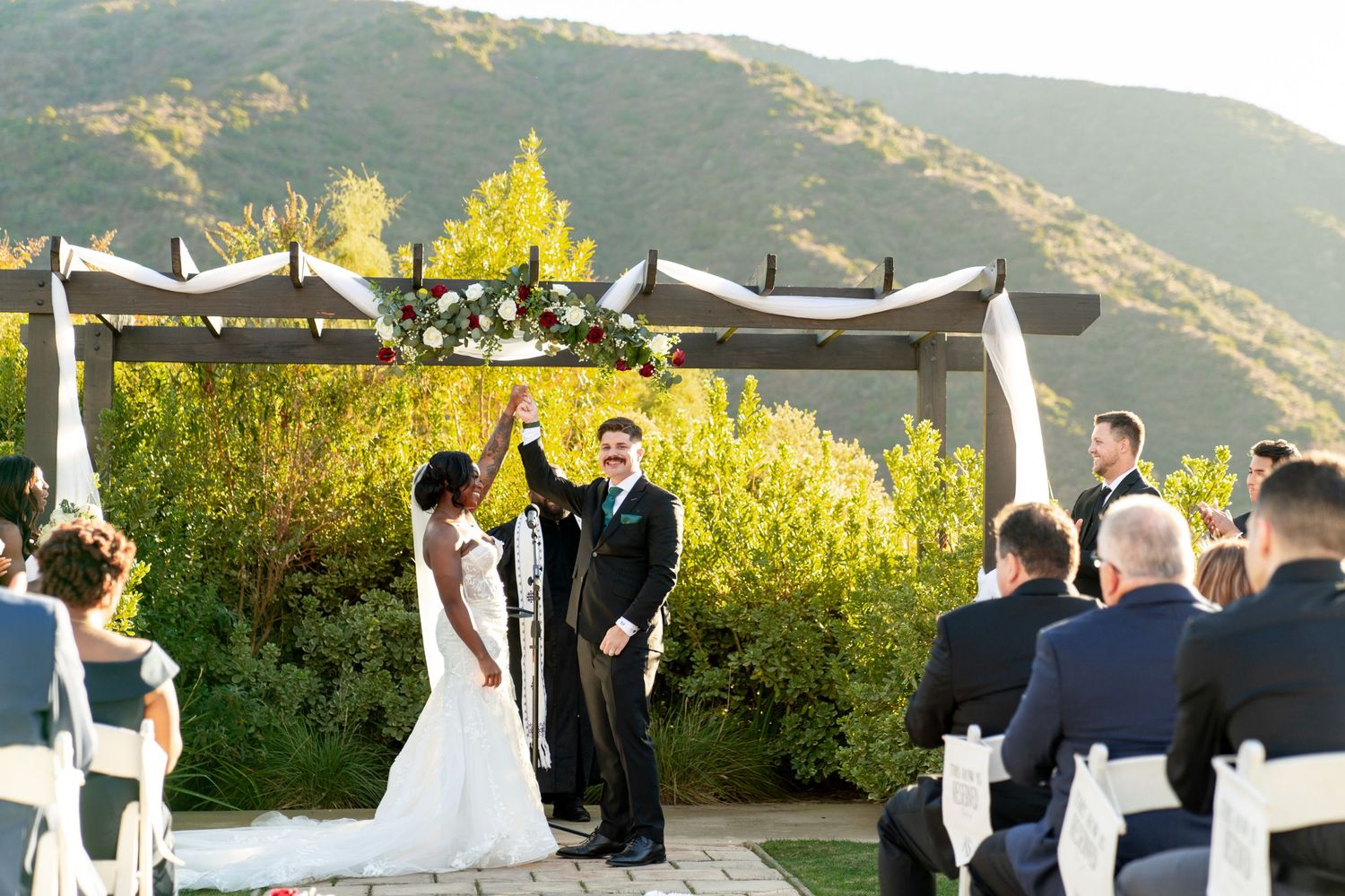 Outdoor wedding ceremony with mountain views and white chairs.