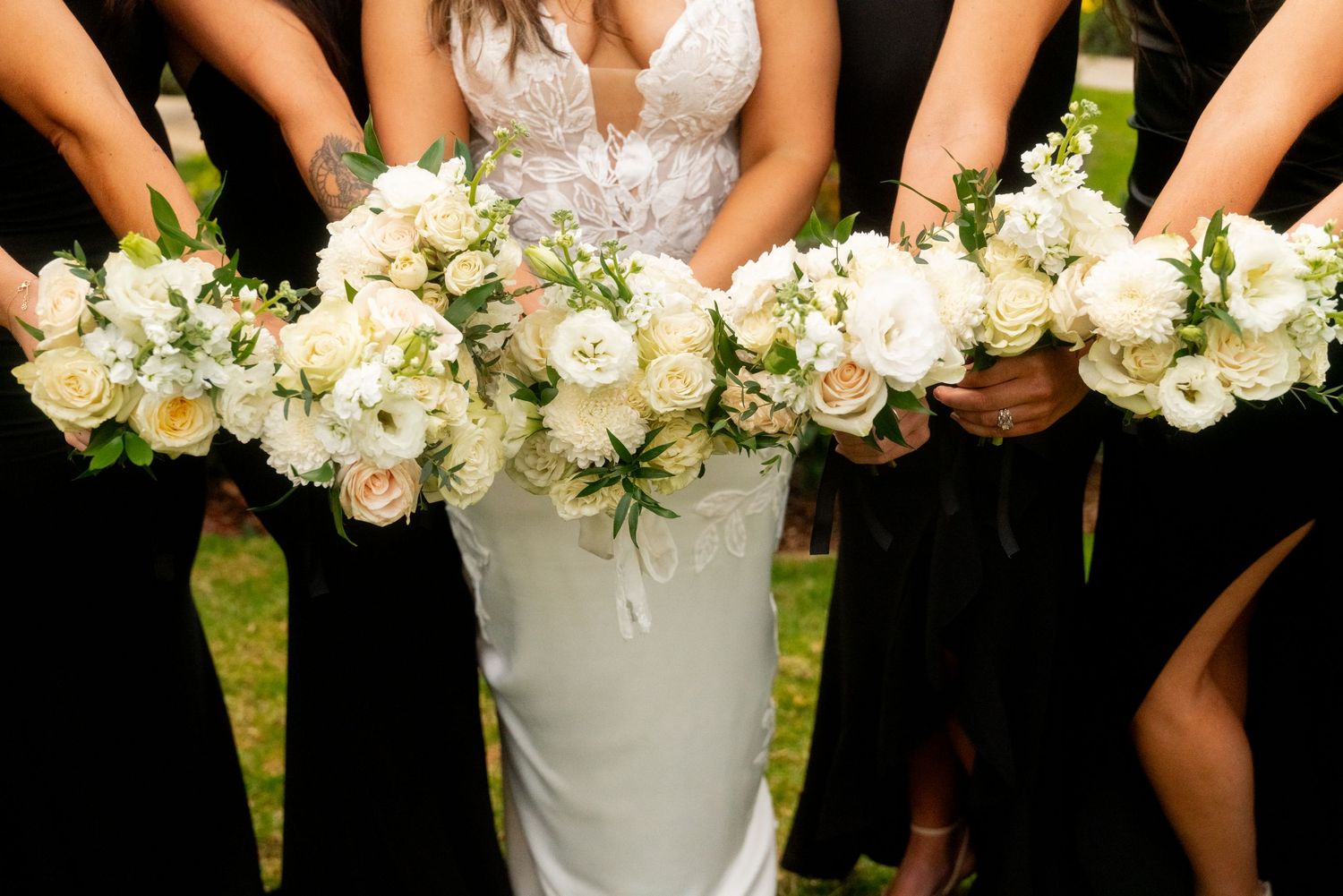 Wedding party holds elegant white floral bouquets with roses and greenery against black and white dresses.