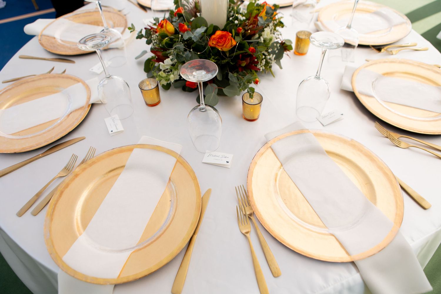 Elegant wedding table setting with gold charger plates and colorful floral centerpiece.