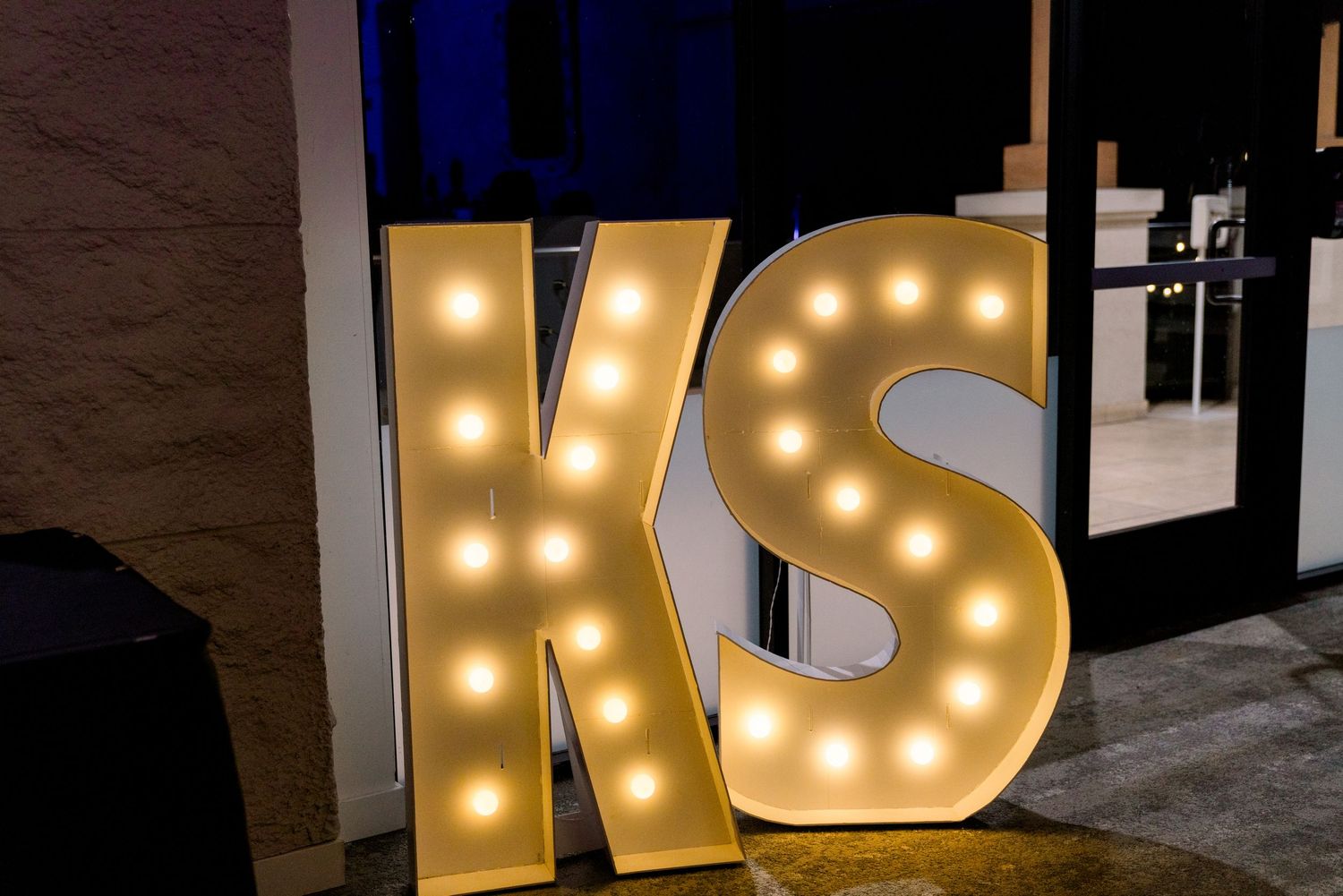Illuminated marquee letters 'KS' glow warmly against a dark wall.