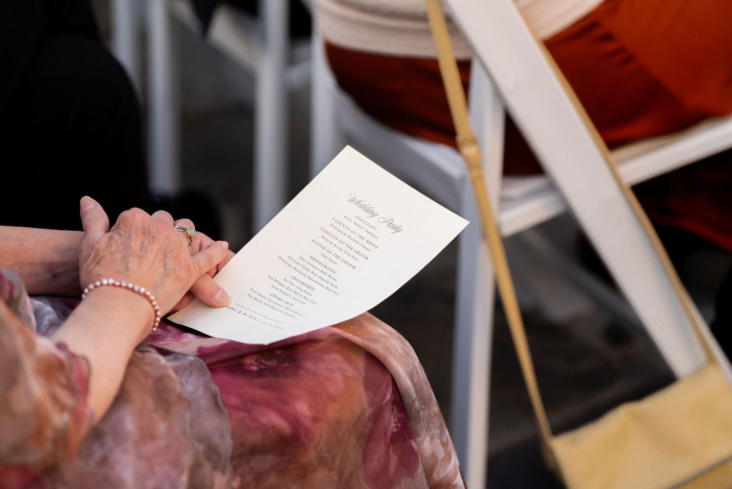 Someone reading a paper document in a pink dress during what appears to be a formal event.