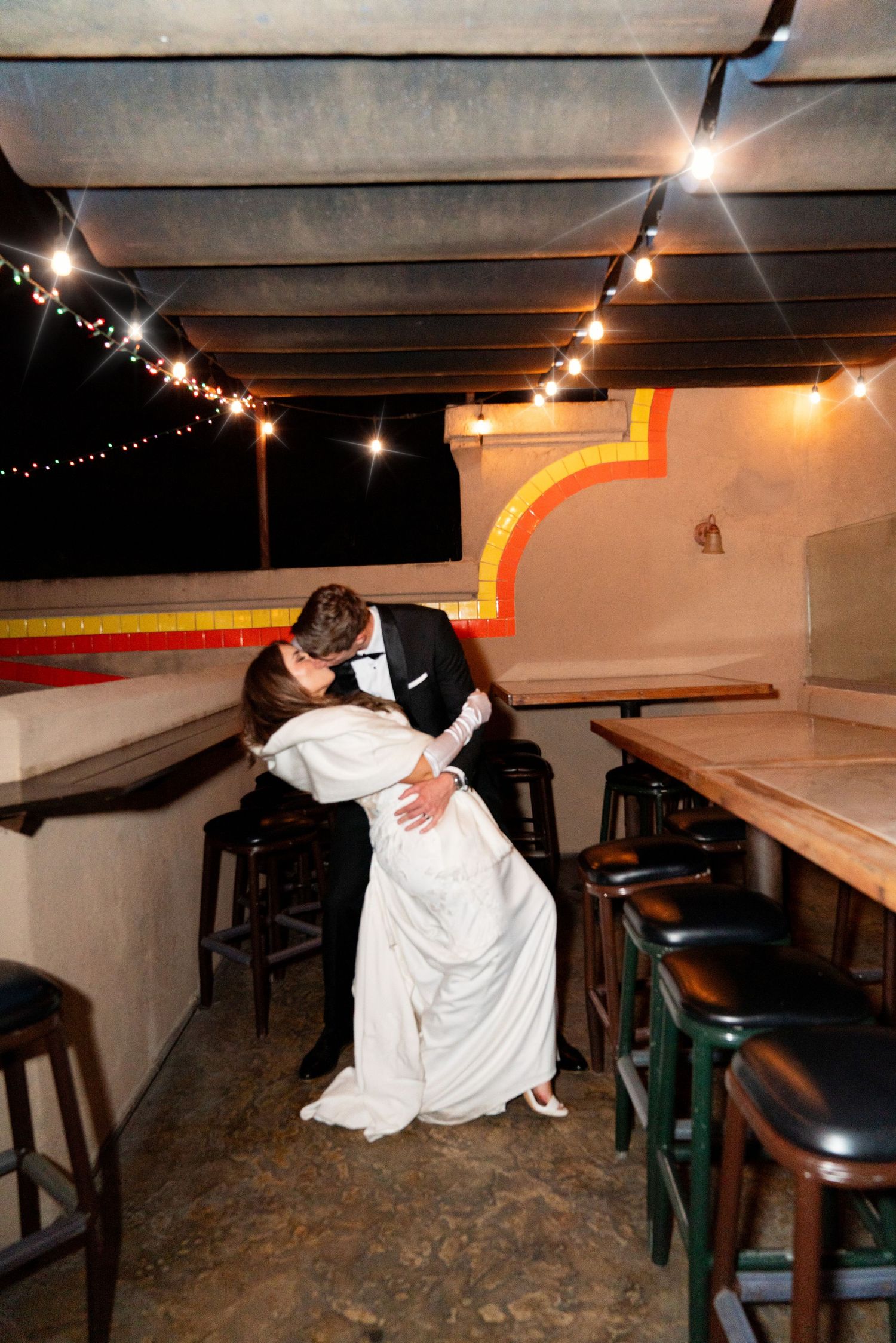 Romantic dip pose between couple under string lights in rustic venue setting.