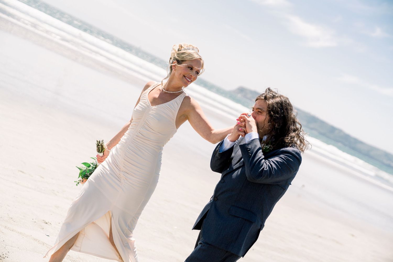 A couple shares a joyful candid moment while walking together on a sunny beach.