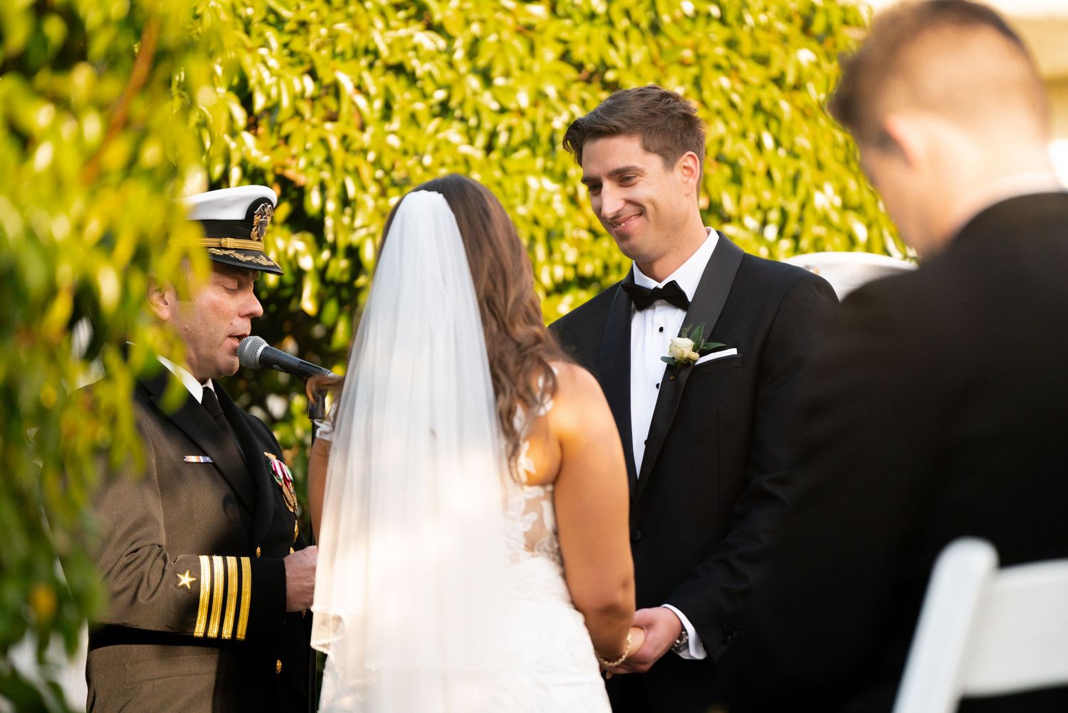 A military wedding ceremony taking place outdoors with yellow foliage in the background.