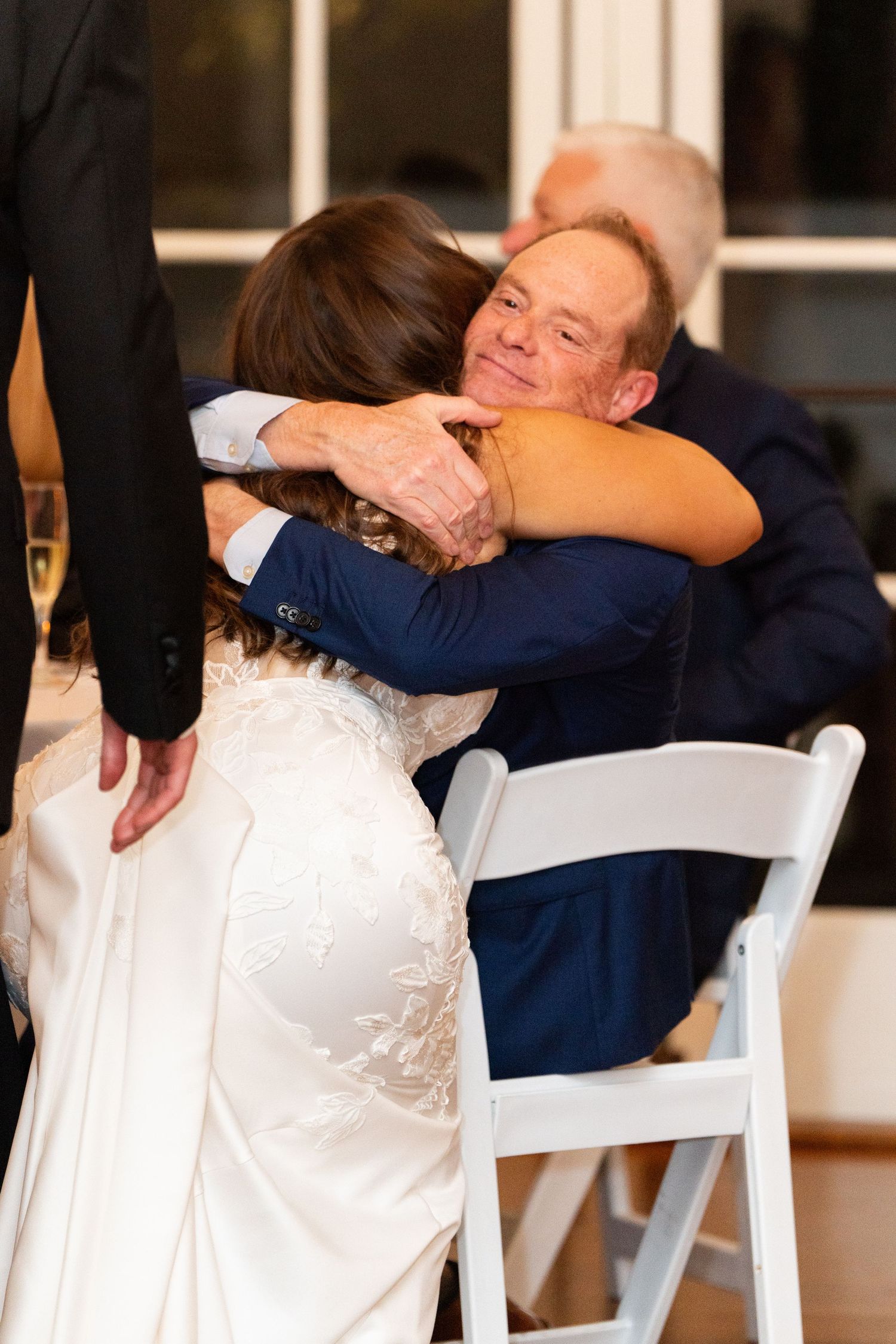 A tender embrace between two people at a wedding reception, with the bride wearing a white lace dress.