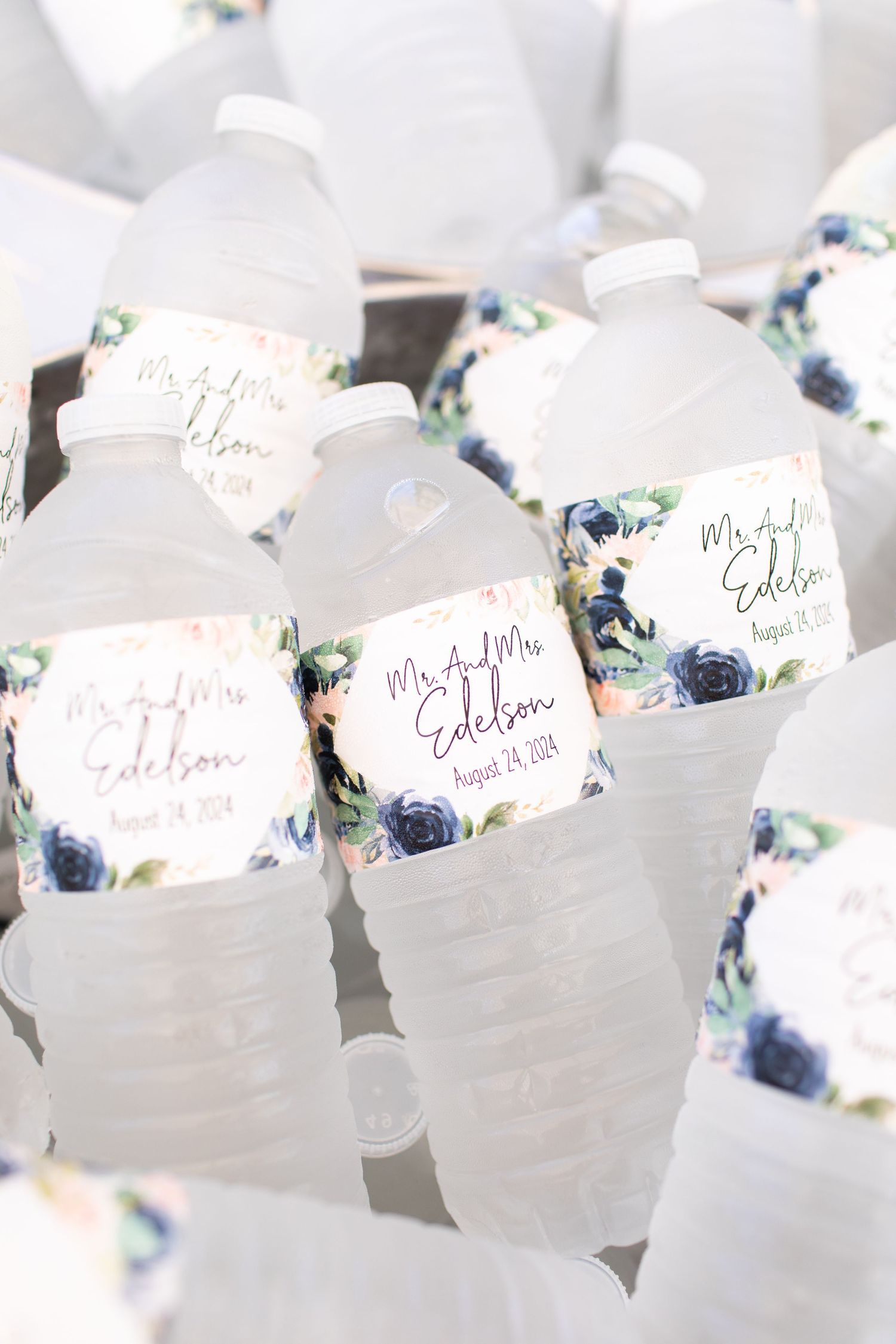 Customized water bottles with elegant floral labels featuring navy blue roses and decorative text for a wedding celebration.