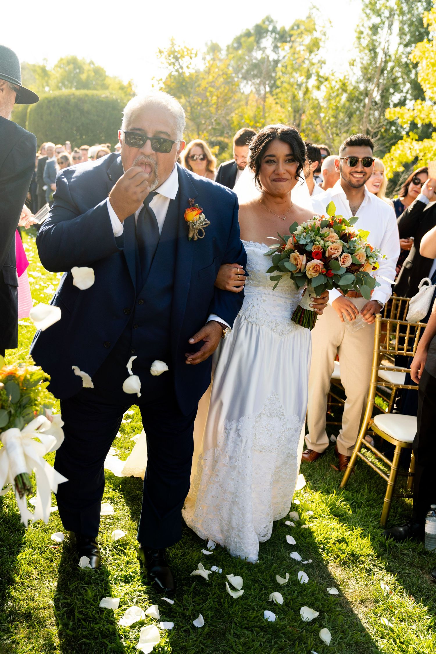 Wedding ceremony in a garden setting with white petals scattered on lush green grass.